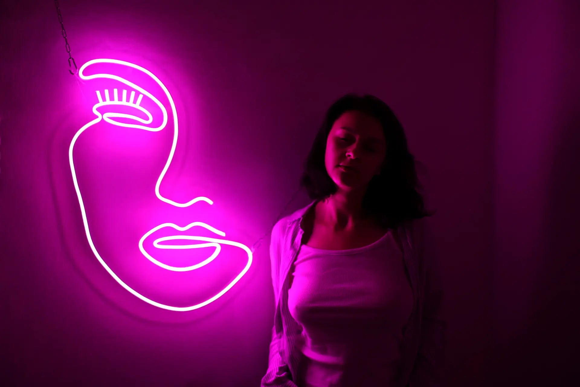 A bright pink neon sign of a girls face with a women standing next to it