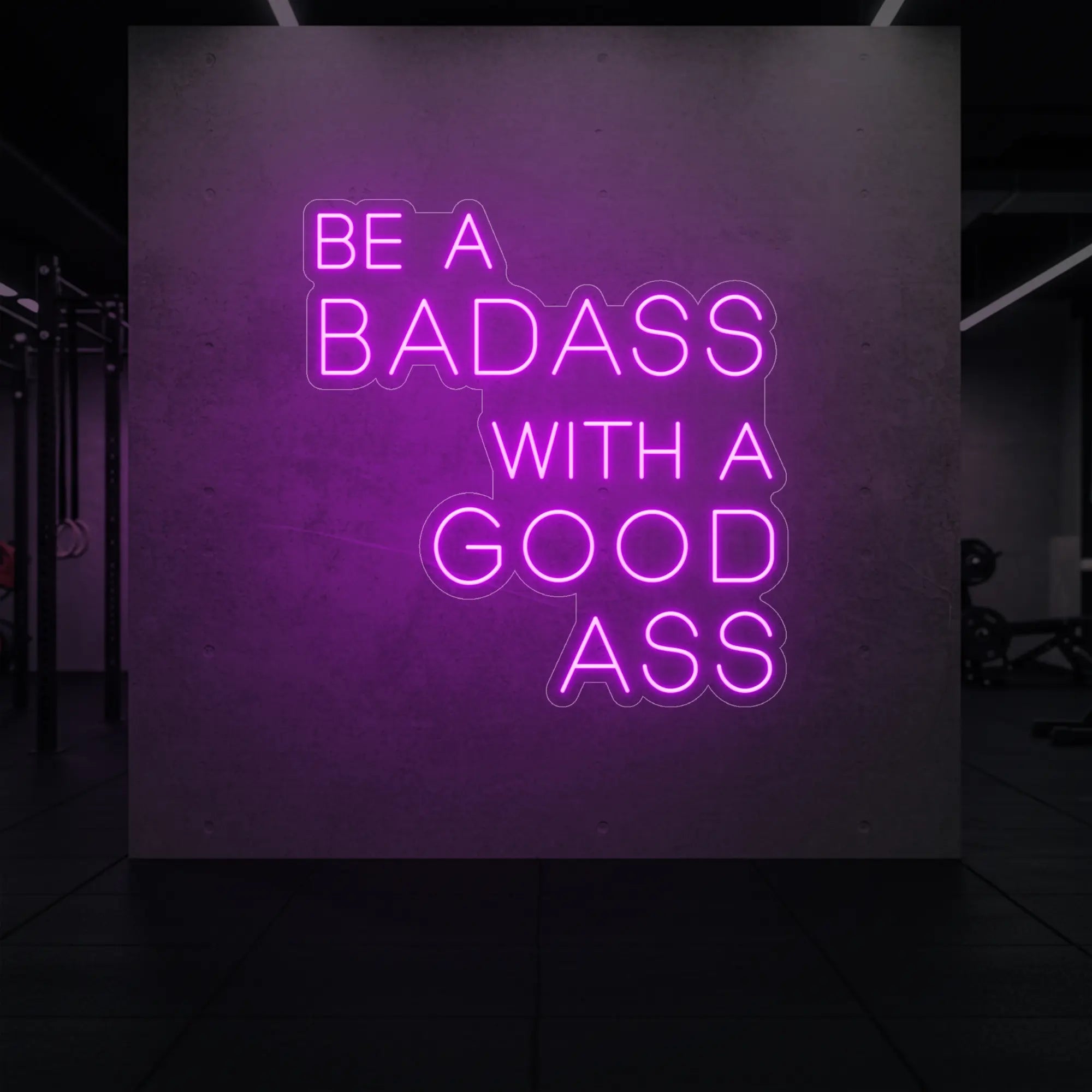'Be a Badass With a Good Ass' neon sign glowing in deep pink against a styled interior wall.