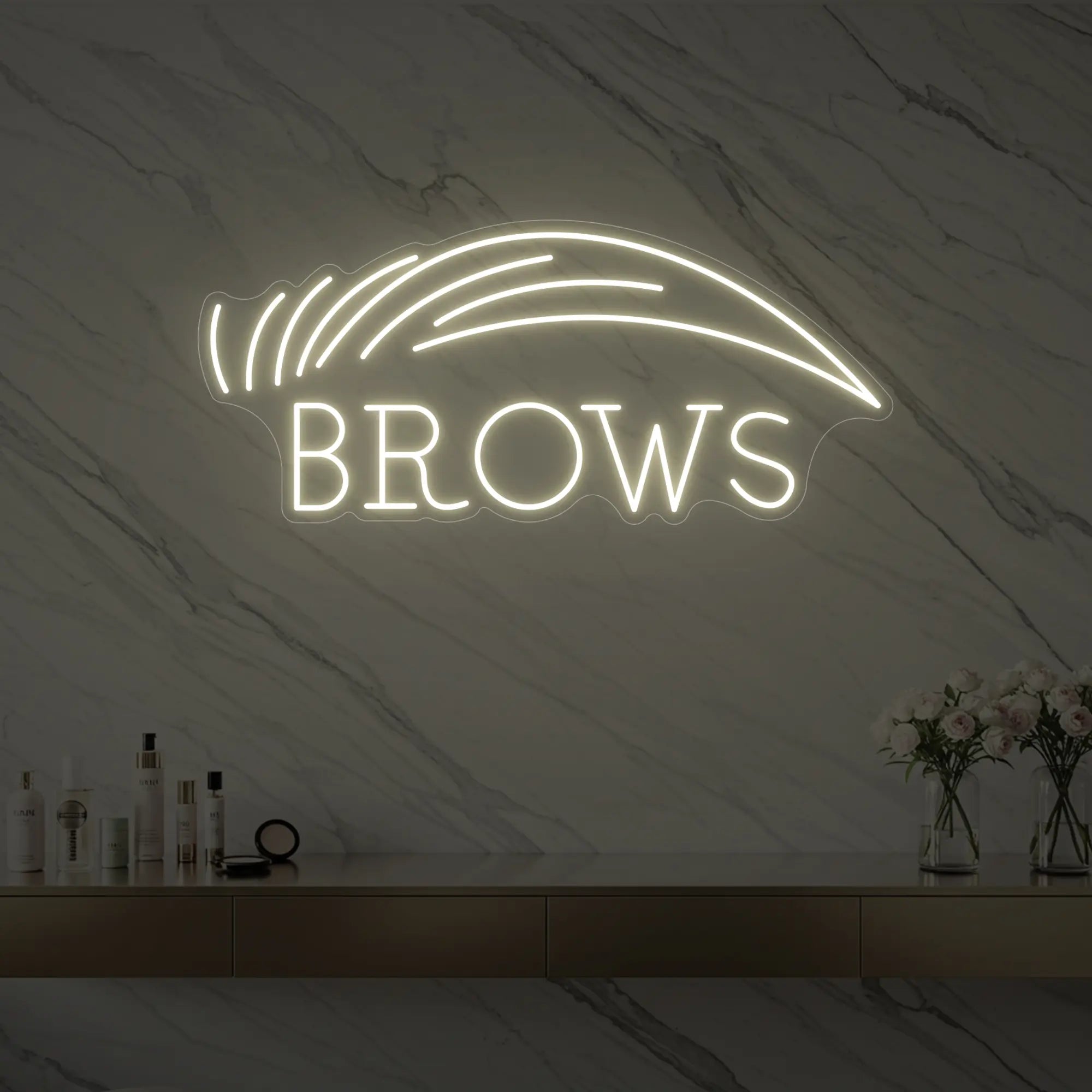 Photo of the 'BROWS' neon sign with an eyebrow graphic glowing in warm white against a styled interior wall.
