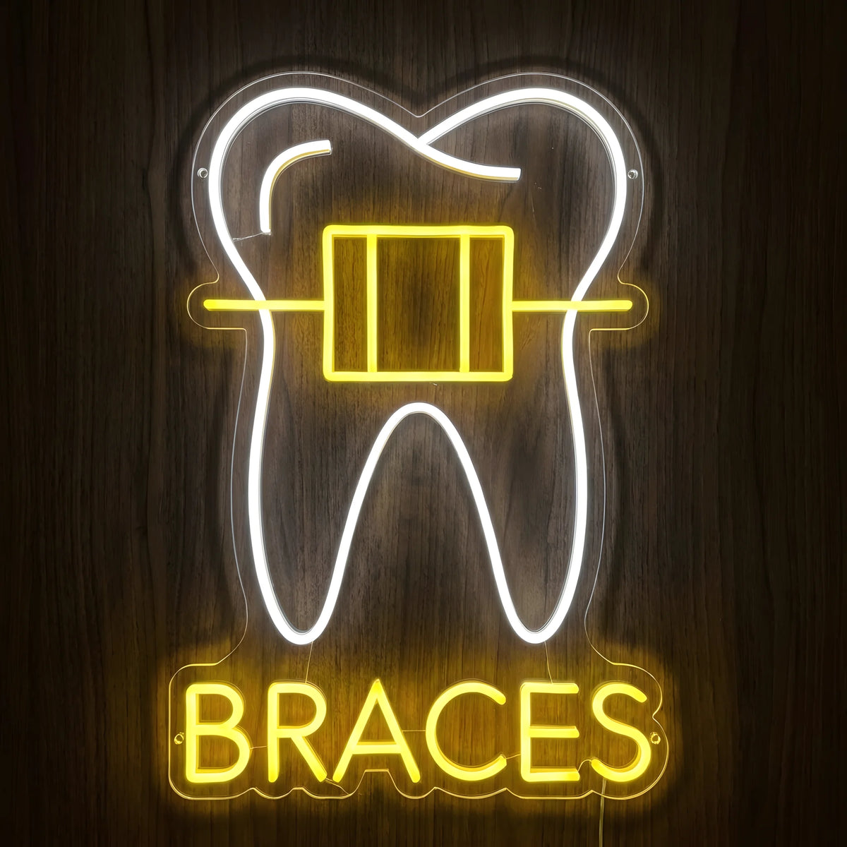 Dental Braces LED neon sign featuring a glowing white tooth outline with yellow orthodontic braces and BRACES lettering on clear acrylic backing against a dark wooden wall.
