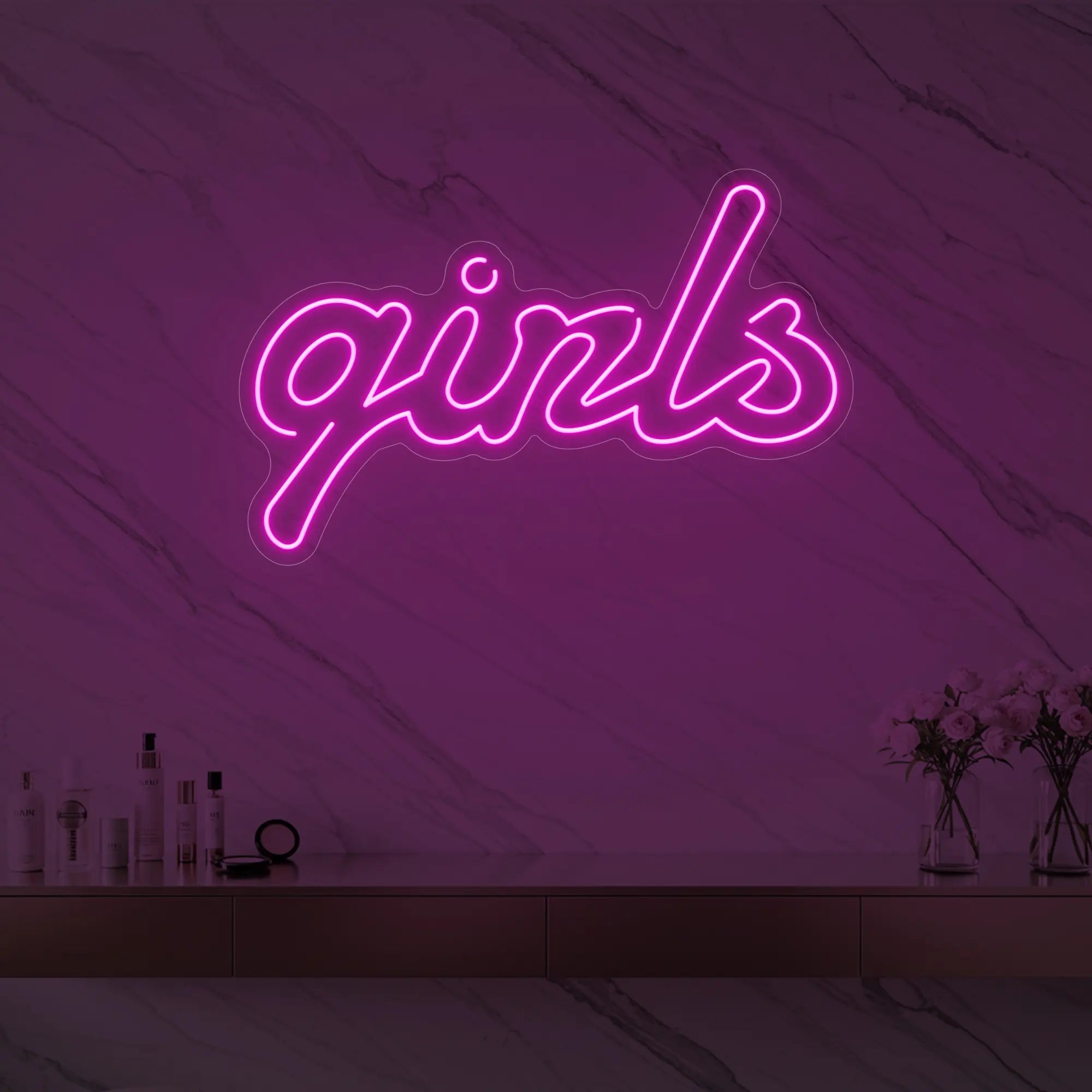 Photo of the 'girls' neon sign in playful script glowing in light pink against a styled interior wall.
