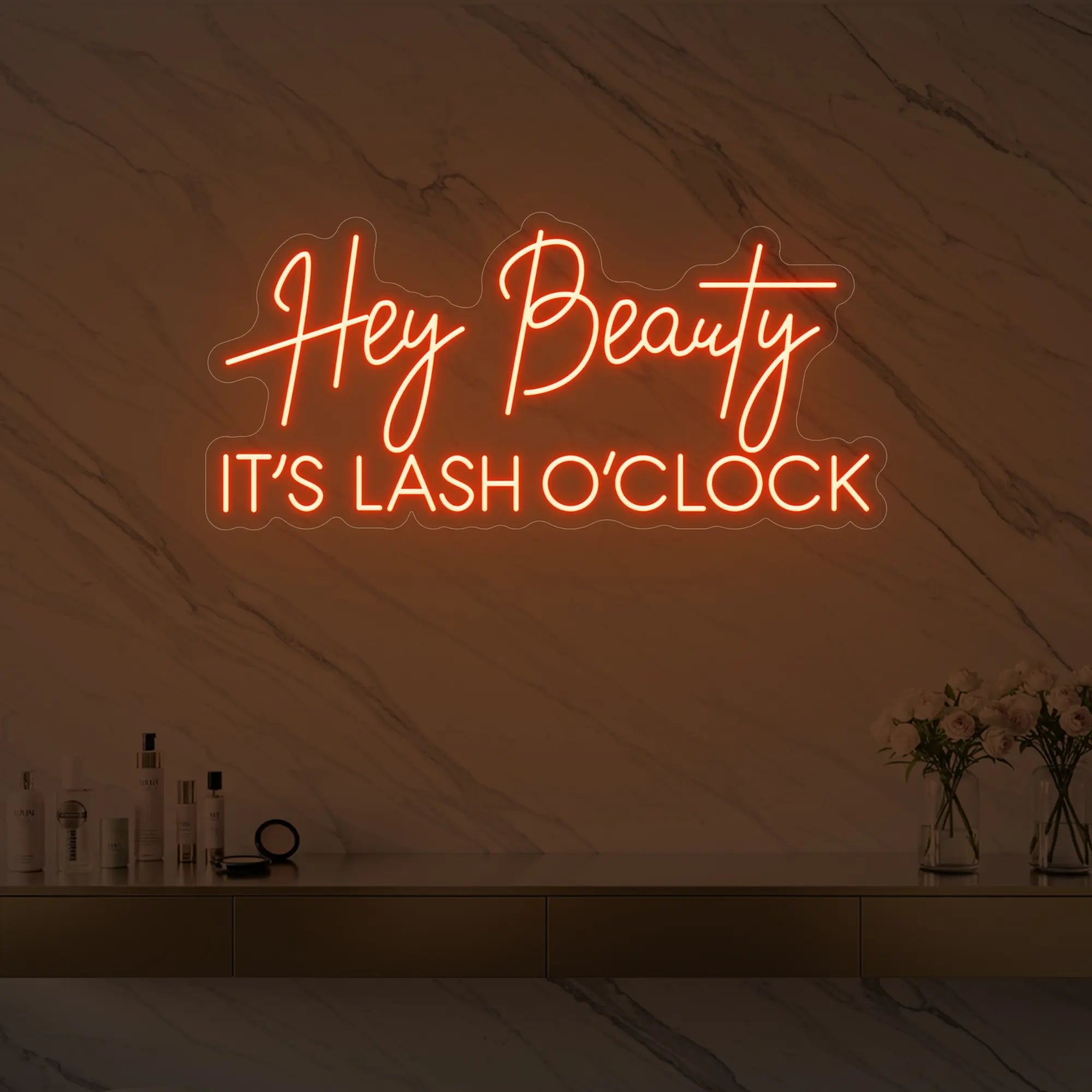 Photo of the 'Hey Beauty IT’S LASH O’CLOCK' neon sign glowing in golden yellow against a styled interior wall.