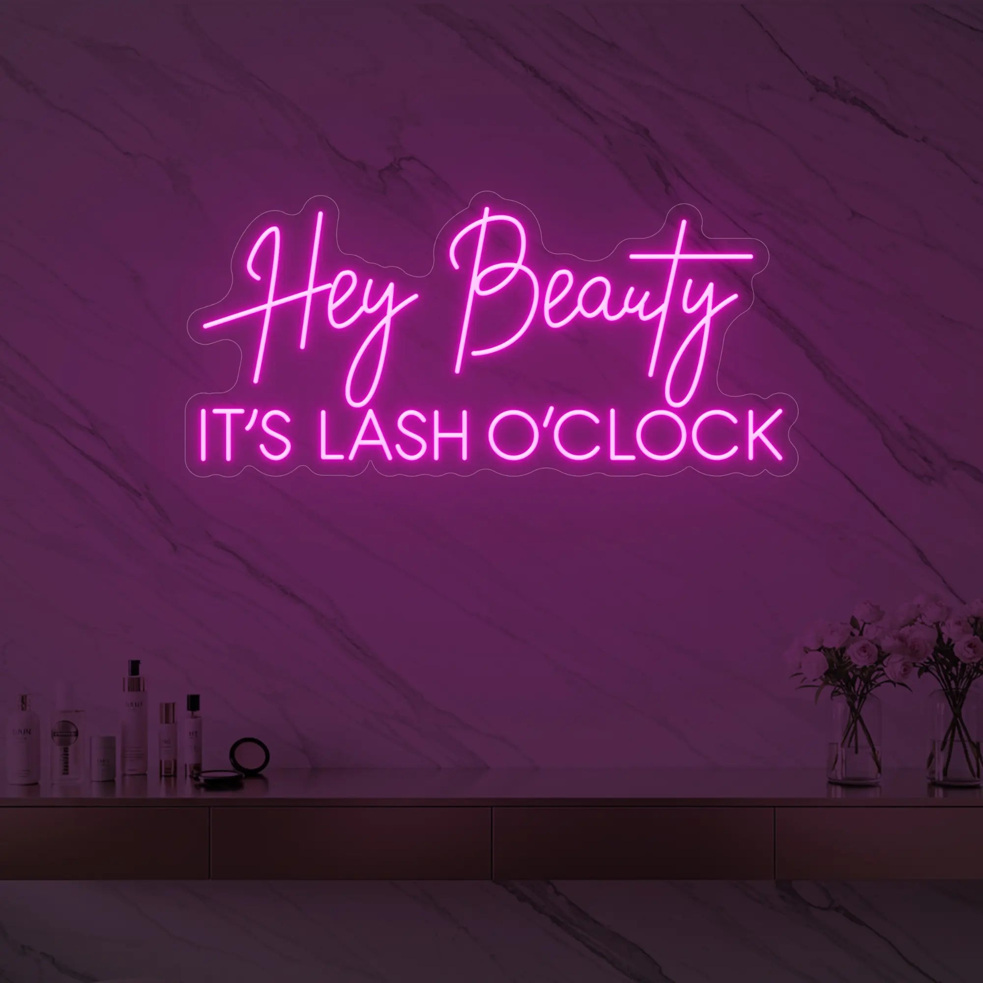 Photo of the 'Hey Beauty IT’S LASH O’CLOCK' neon sign glowing in light pink against a styled interior wall.