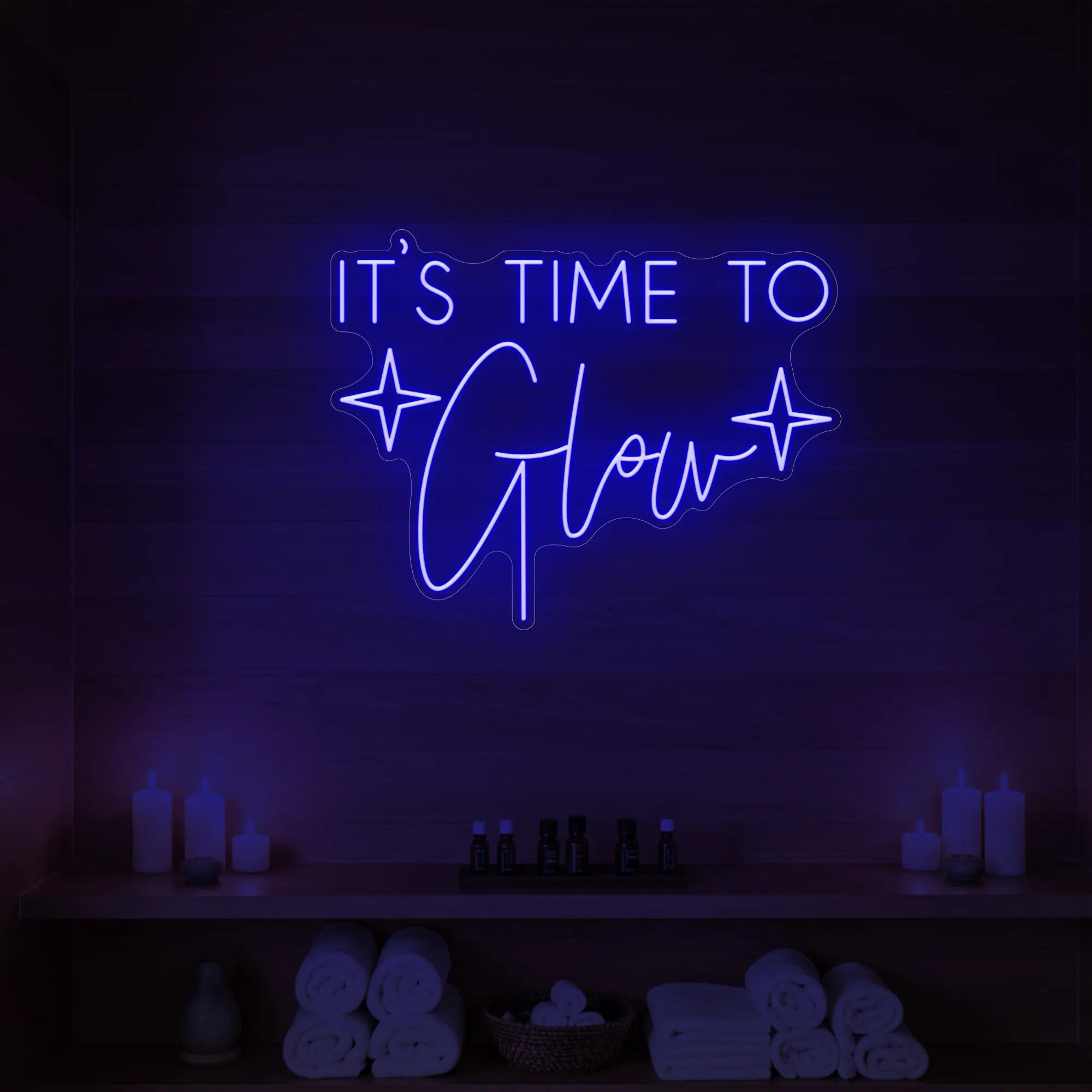 Photo of the 'IT’S TIME TO Glow' neon sign with sparkle icons glowing in deep blue against a styled interior wall.