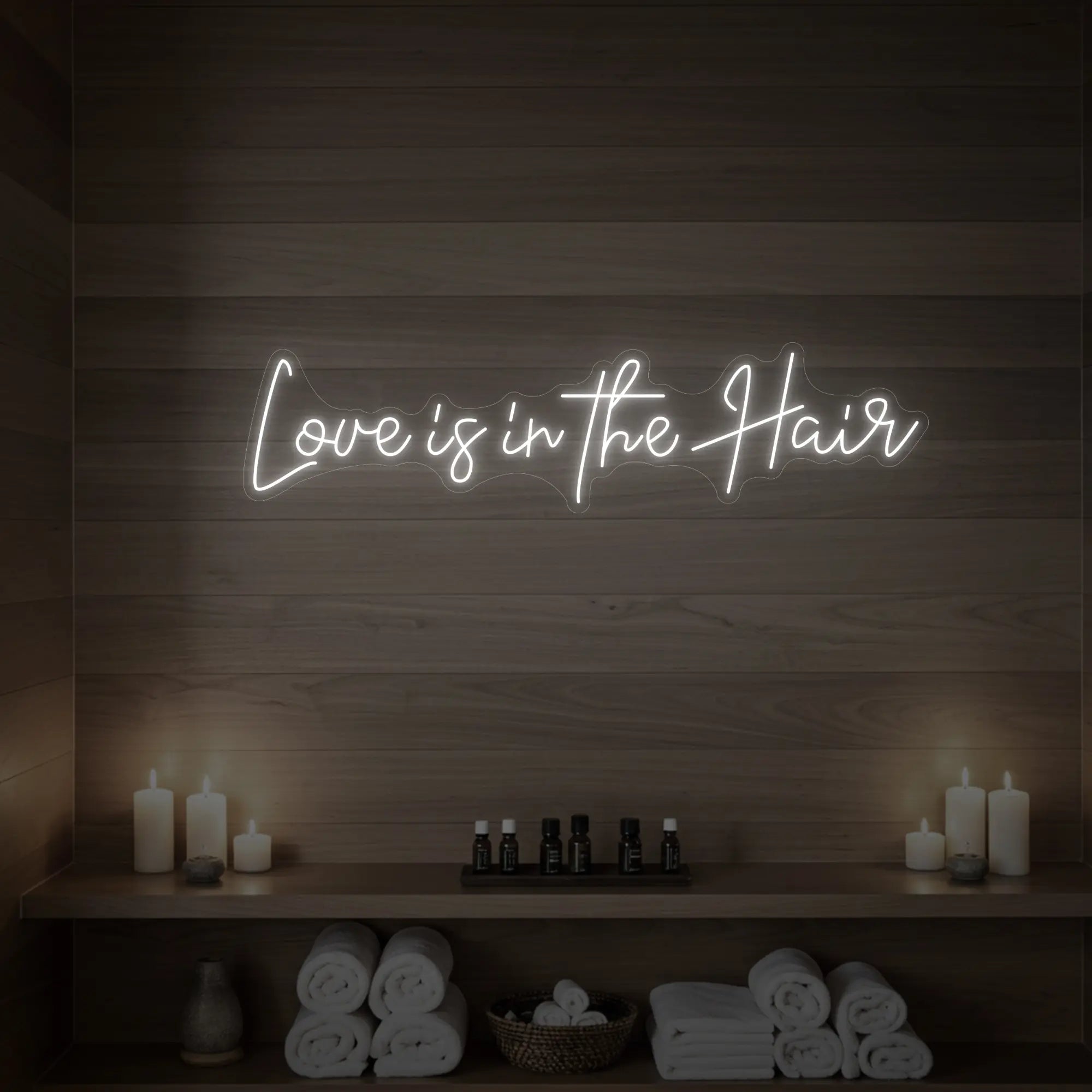 Photo of the 'Love is in the Hair' neon sign glowing in cool white against a styled interior wall.