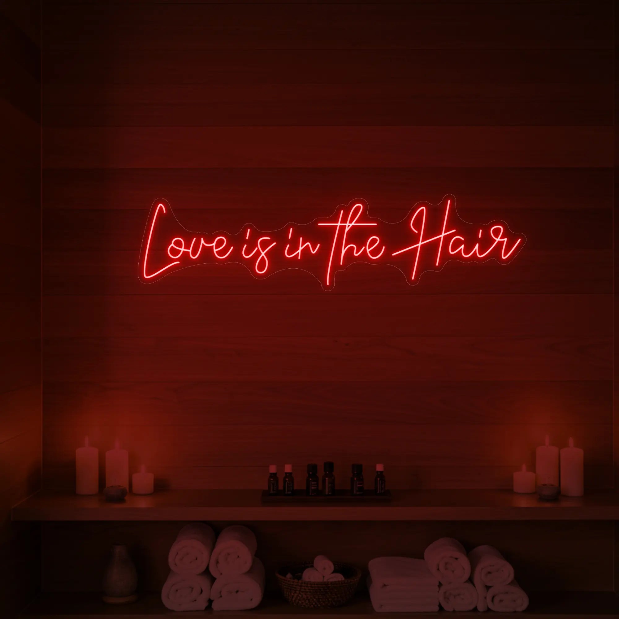Photo of the 'Love is in the Hair' neon sign glowing in red against a styled interior wall.