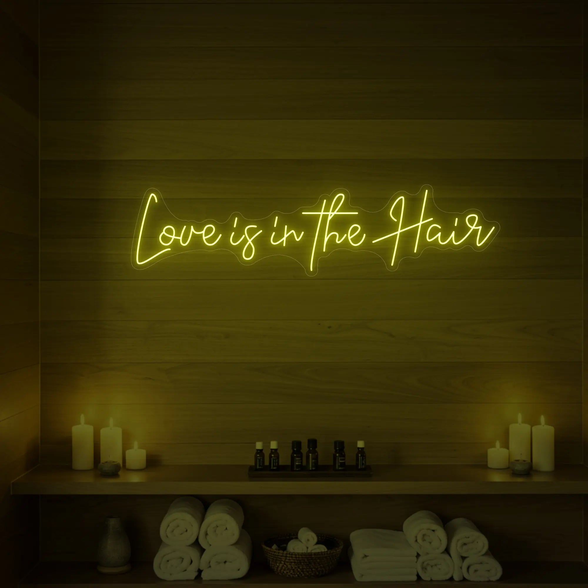 Photo of the 'Love is in the Hair' neon sign glowing in lemon yellow against a styled interior wall.
