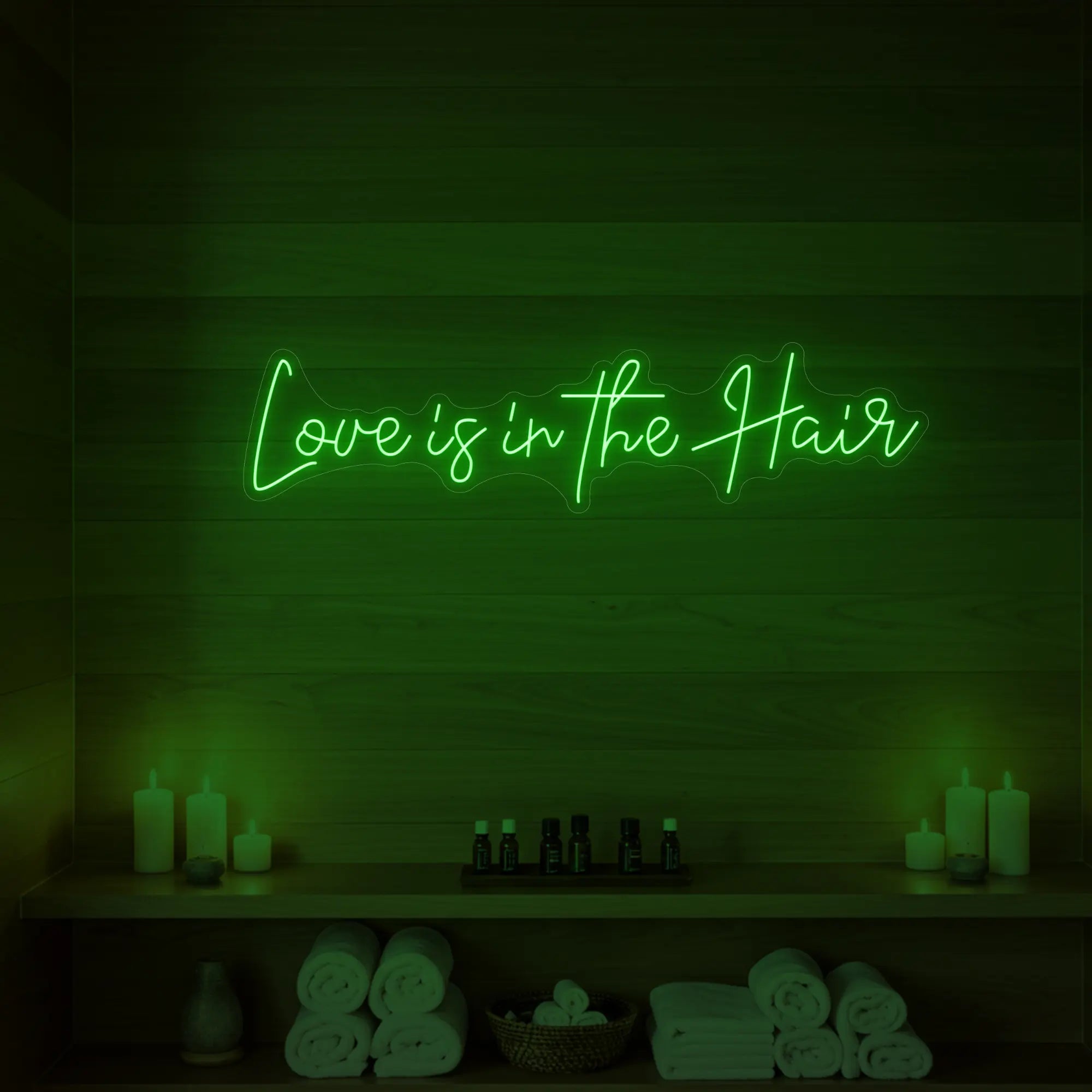 Photo of the 'Love is in the Hair' neon sign glowing in green against a styled interior wall.