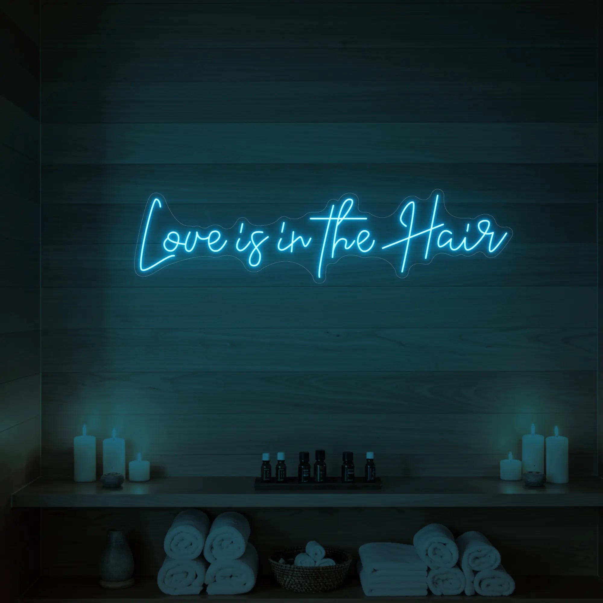 Photo of the 'Love is in the Hair' neon sign glowing in ice blue against a styled interior wall.