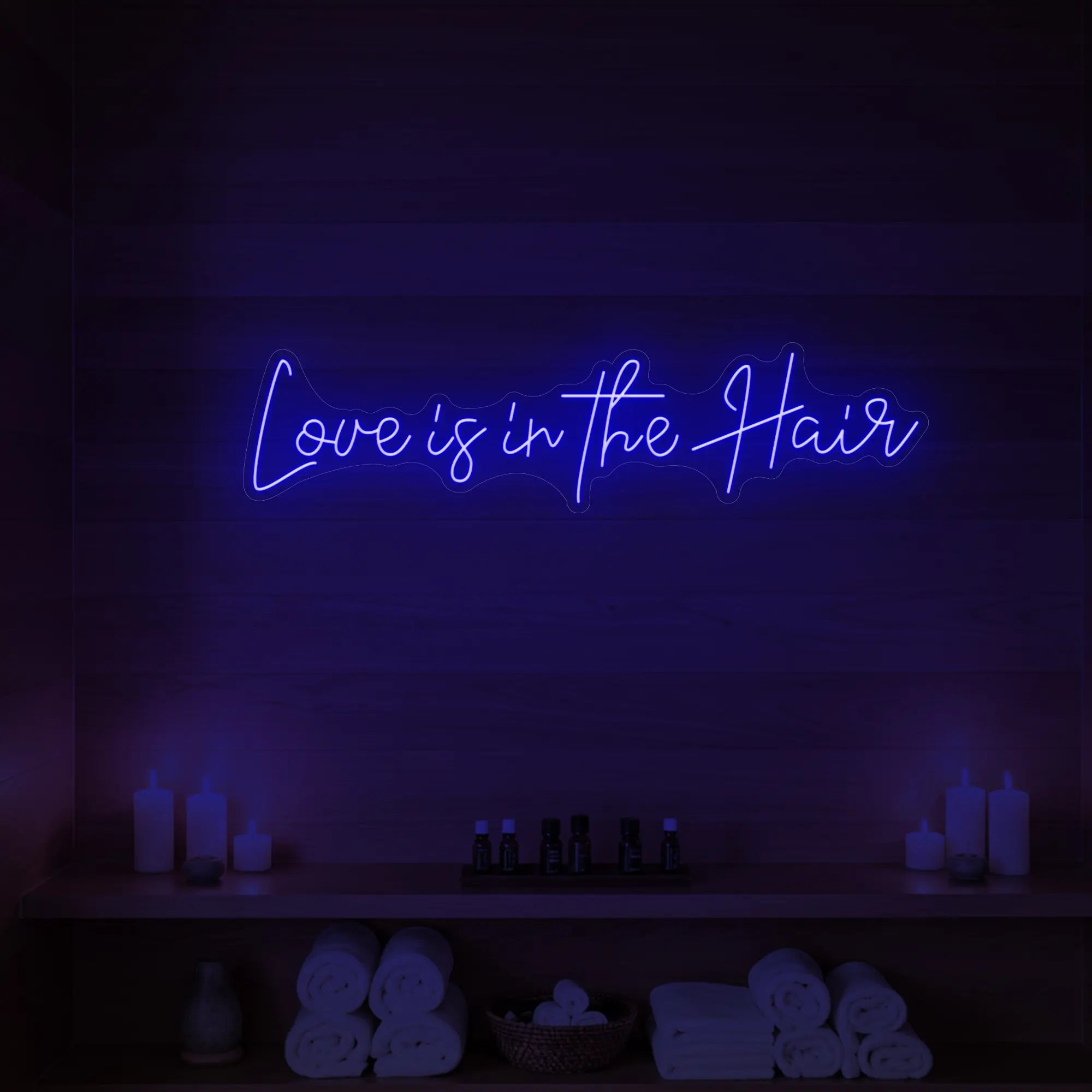 Photo of the 'Love is in the Hair' neon sign glowing in deep blue against a styled interior wall.