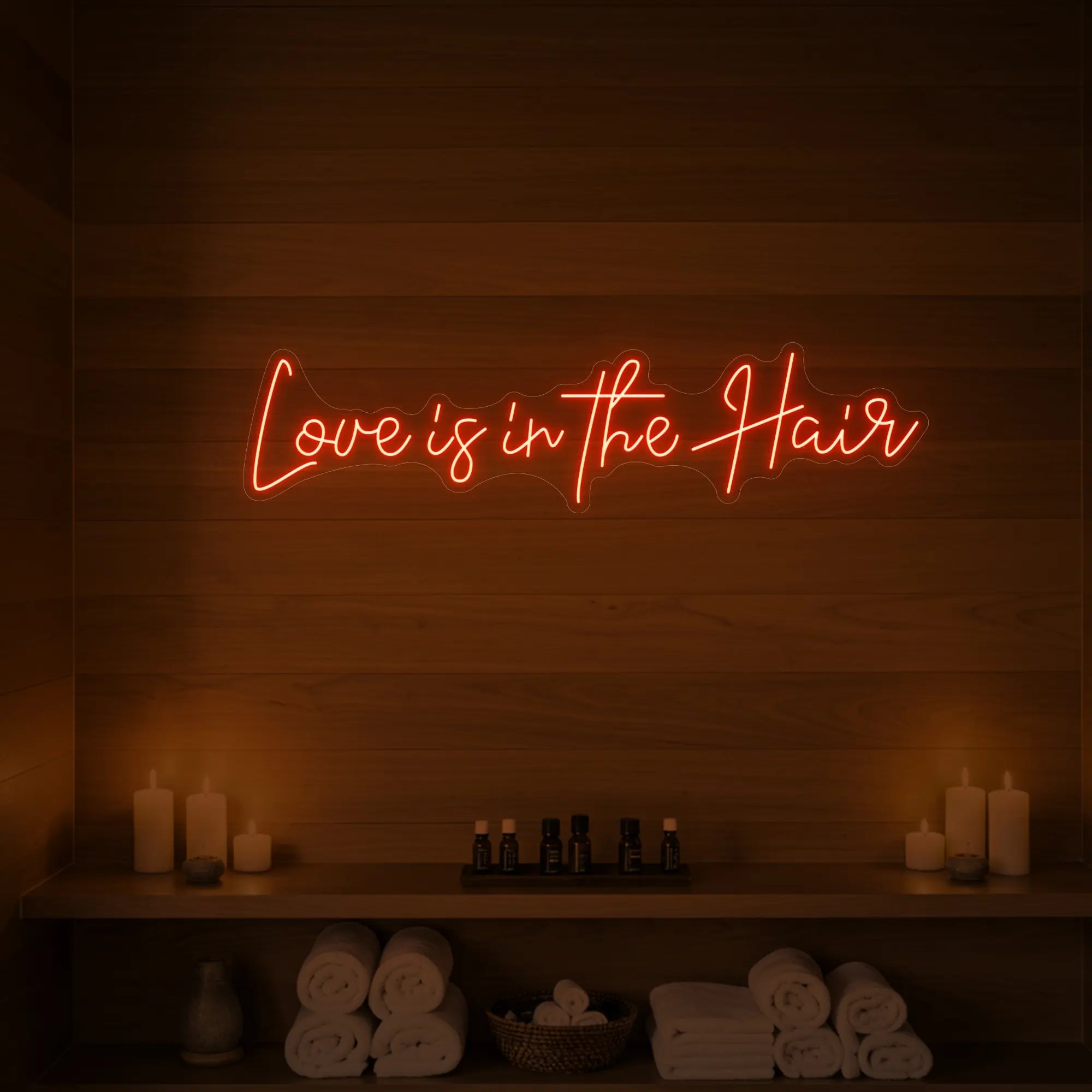 Photo of the 'Love is in the Hair' neon sign glowing in golden yellow against a styled interior wall.