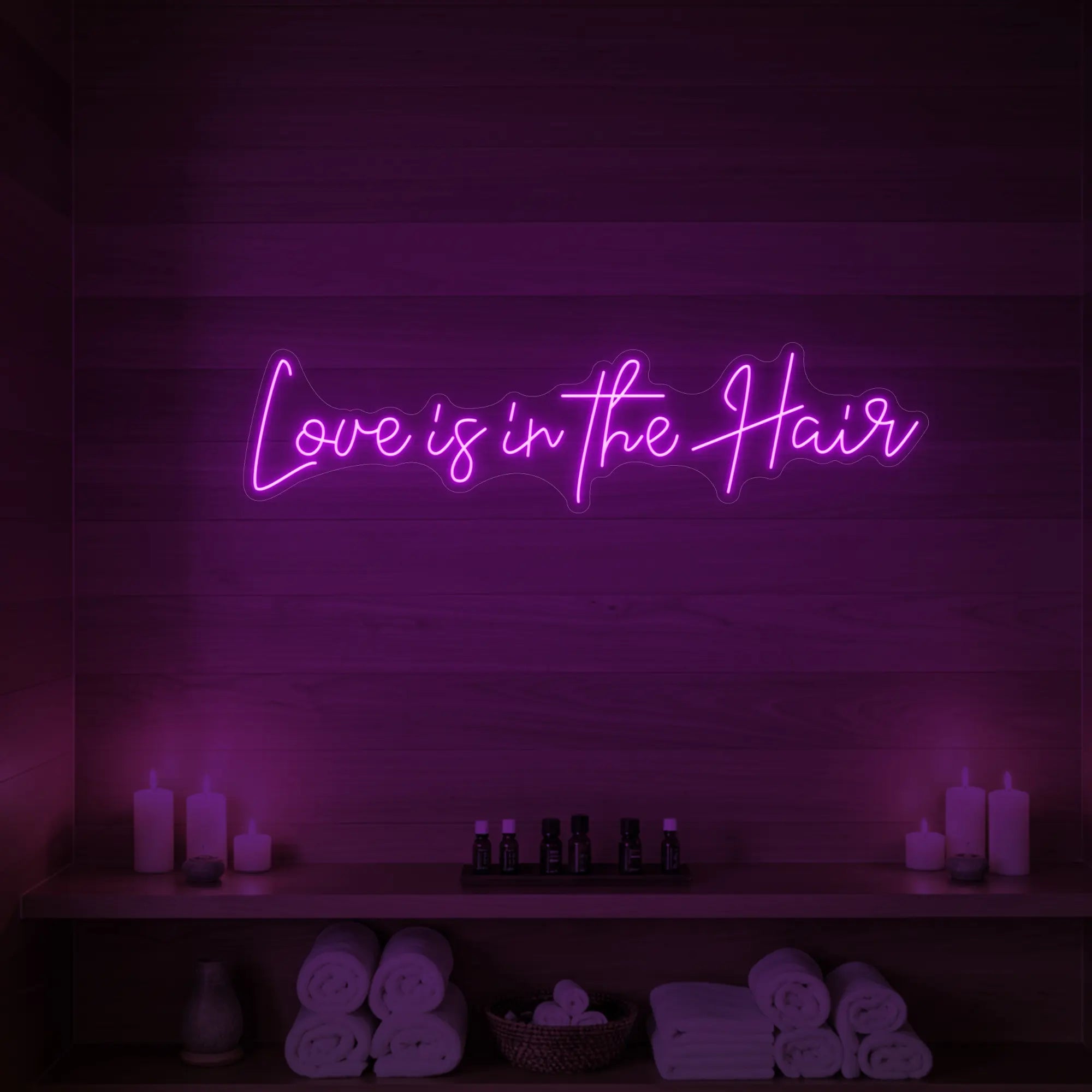 Photo of the 'Love is in the Hair' neon sign glowing in deep pink against a styled interior wall.