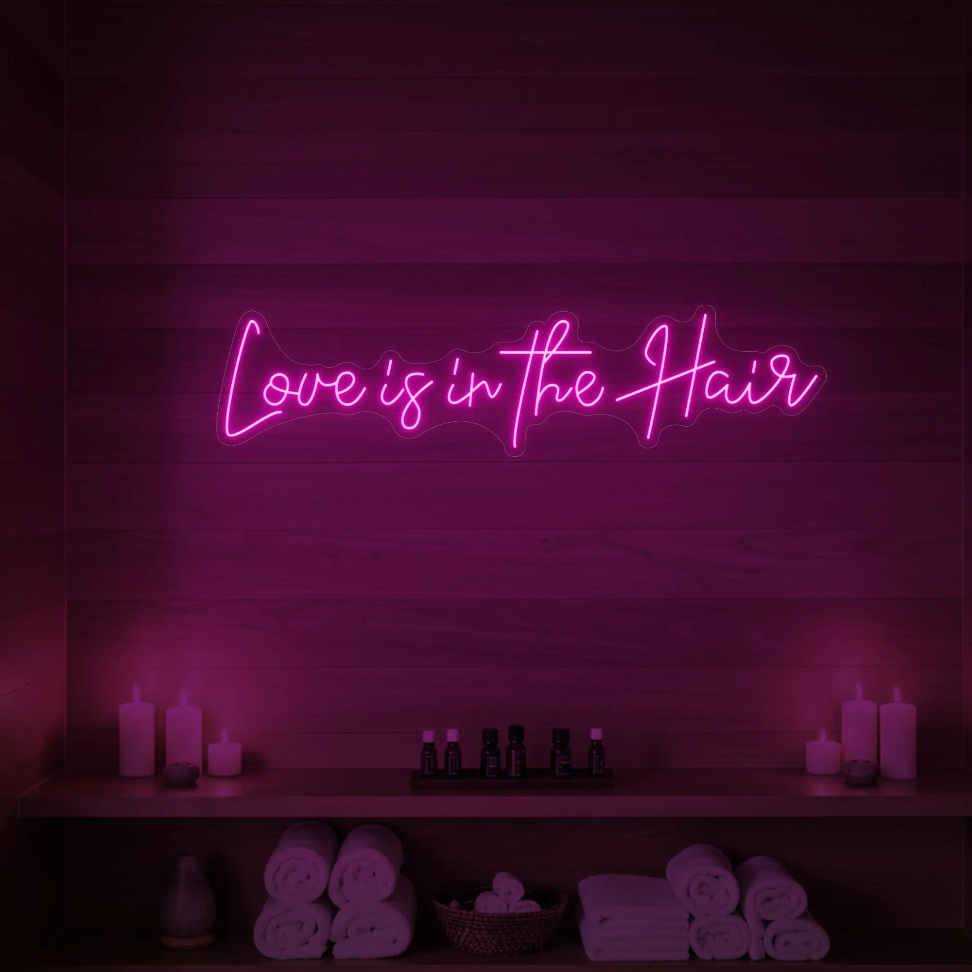 Photo of the 'Love is in the Hair' neon sign glowing in light pink against a styled interior wall.