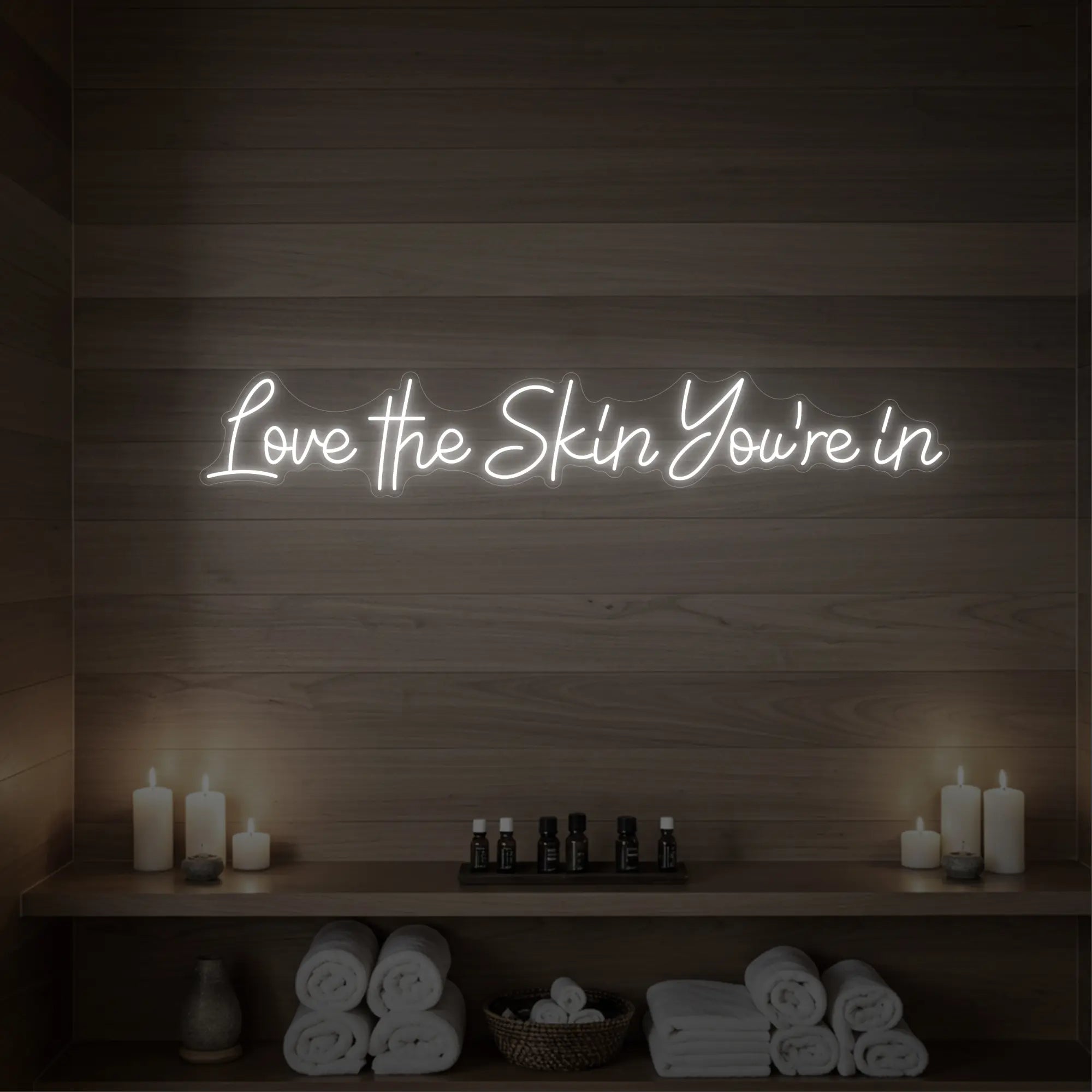 Photo of the 'Love the Skin You're In' neon sign glowing in cool white against a styled interior wall.
