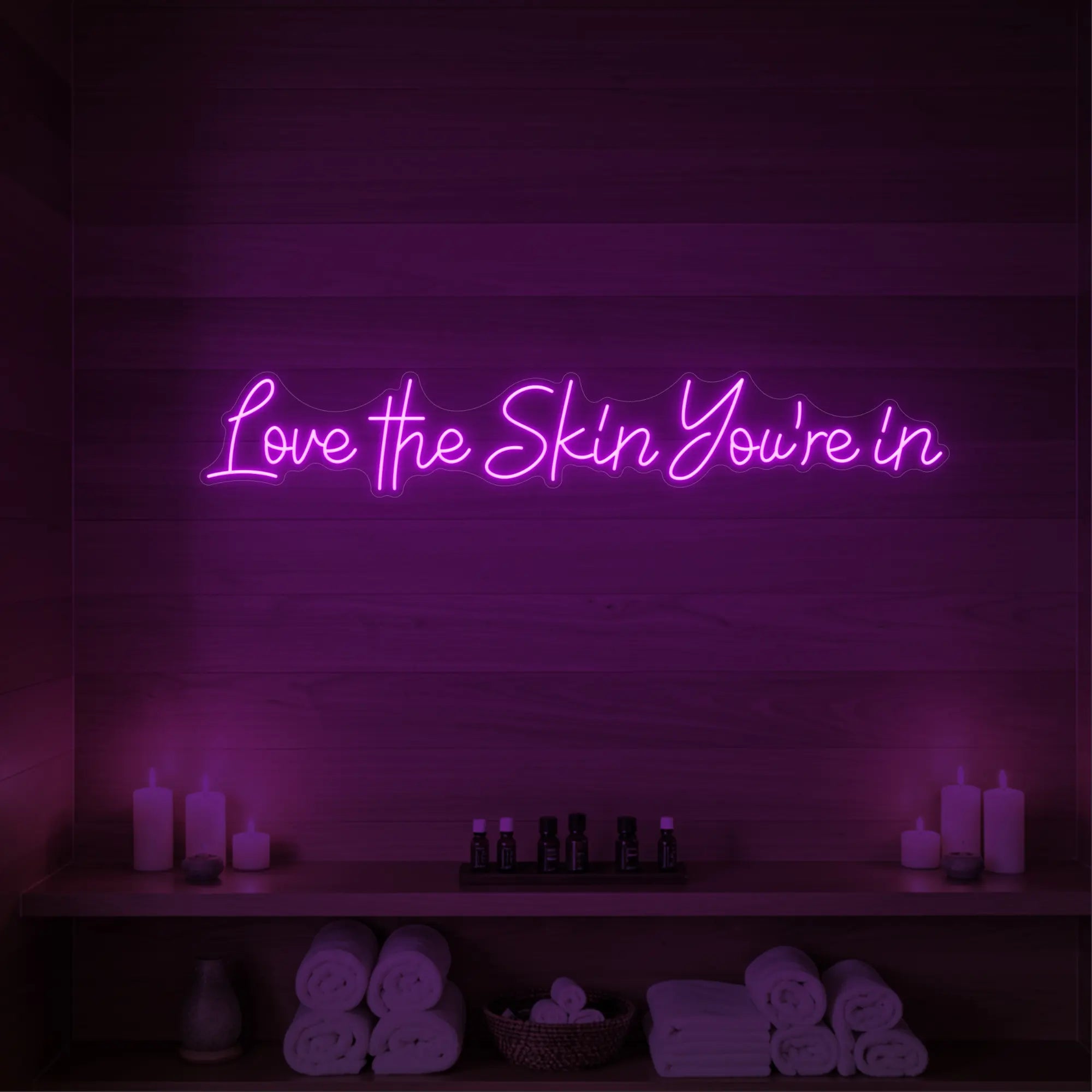 Photo of the 'Love the Skin You're In' neon sign glowing in deep pink against a styled interior wall.