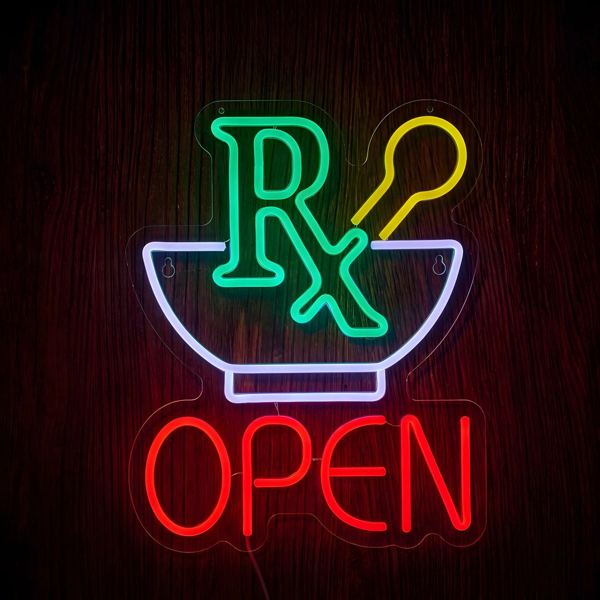Pharmacy Mortar & Pestle Open LED Neon Sign featuring a green Rx symbol, white mortar bowl, yellow pestle, and red OPEN lettering on clear acrylic backing against a dark wooden wall.