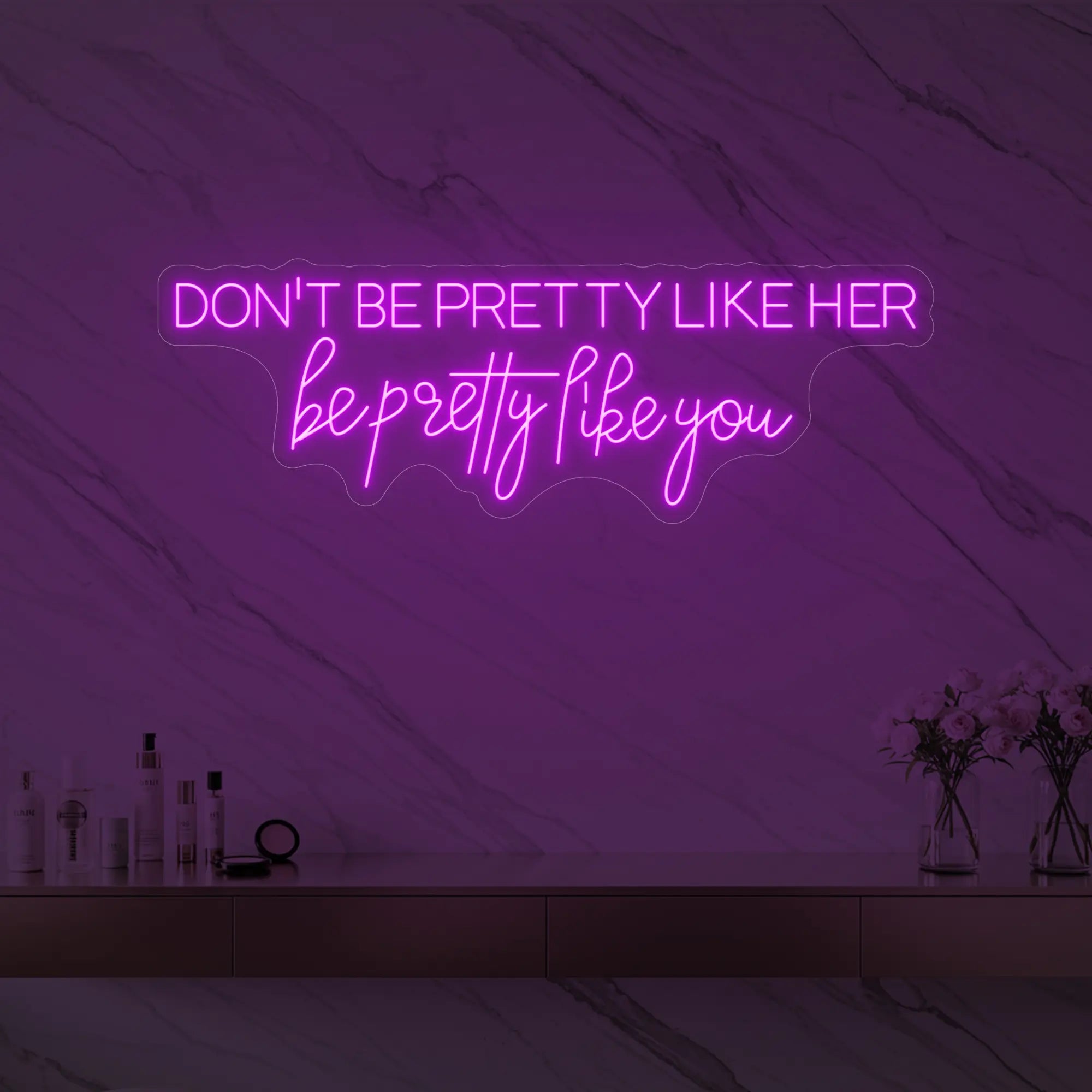 Photo of the 'DON'T BE PRETTY LIKE HER — be pretty like you' neon sign glowing in deep pink against a styled interior wall.