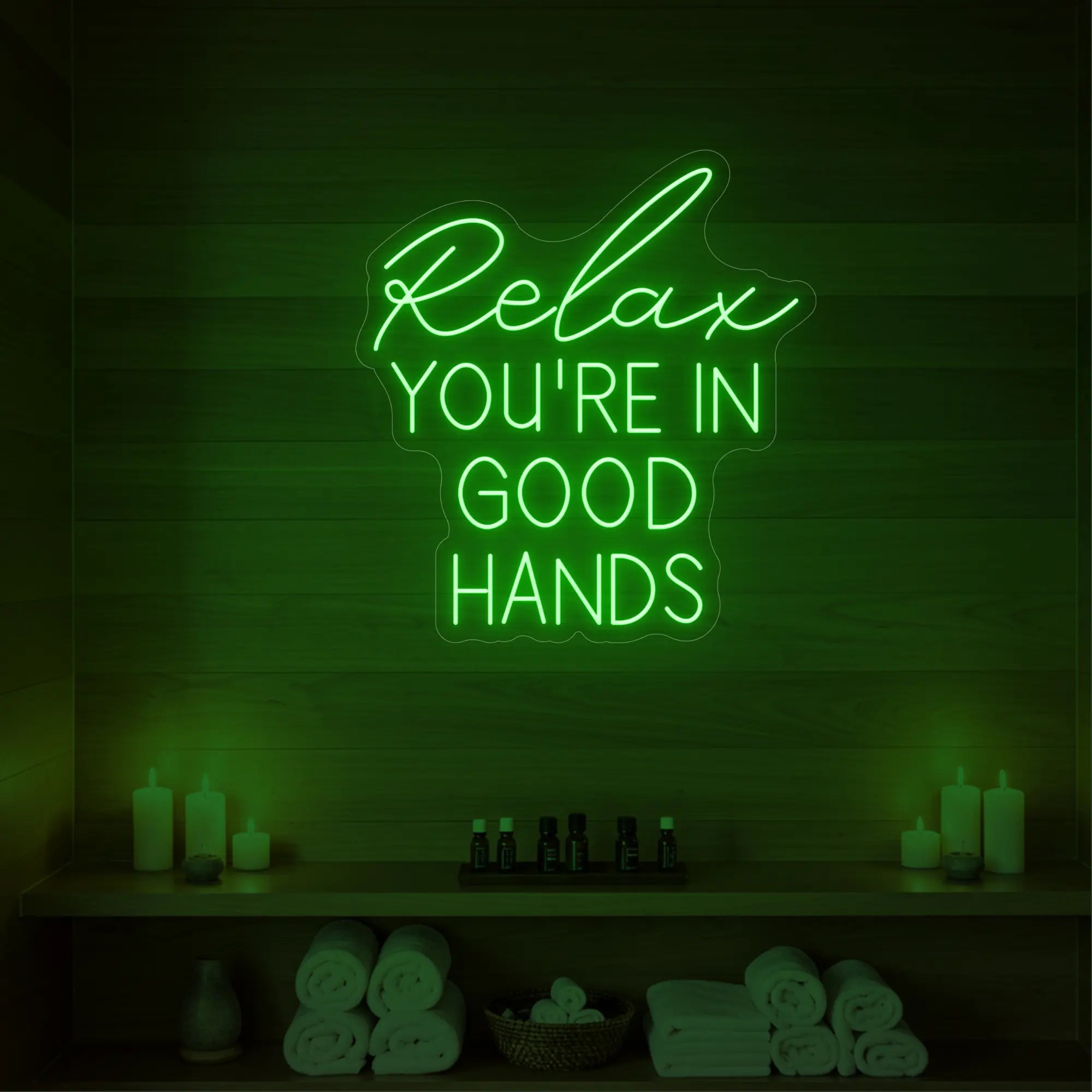 Photo of the 'Relax You're in Good Hands' neon sign glowing in green against a styled interior wall.