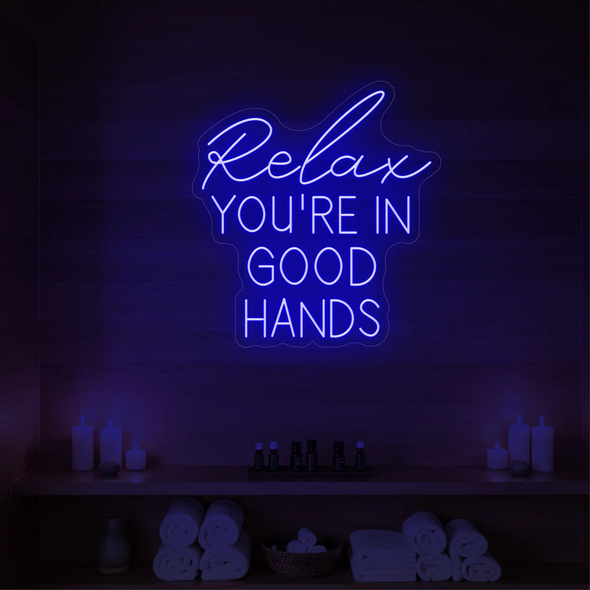Photo of the 'Relax You're in Good Hands' neon sign glowing in deep blue against a styled interior wall.