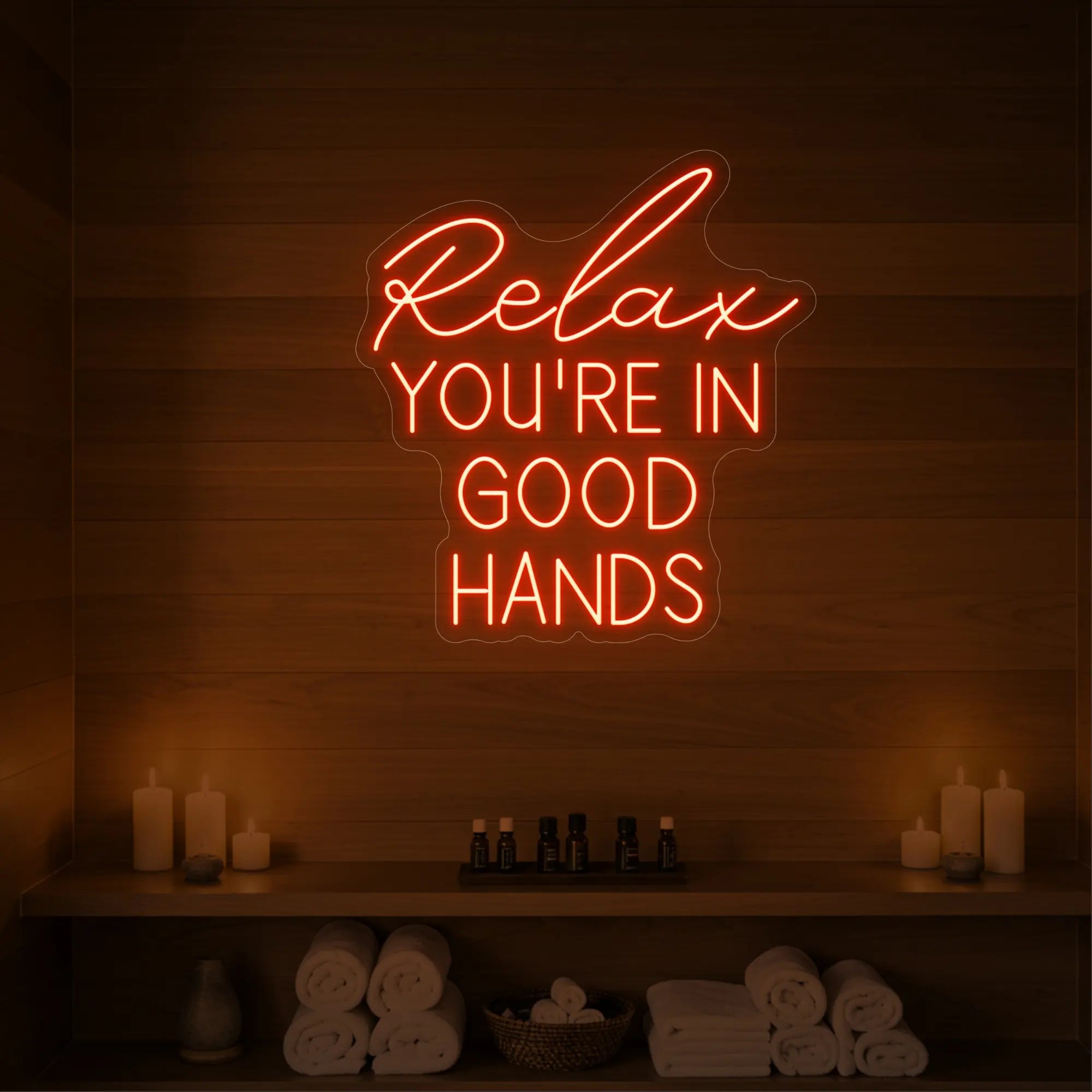 Photo of the 'Relax You're in Good Hands' neon sign glowing in golden yellow against a styled interior wall.