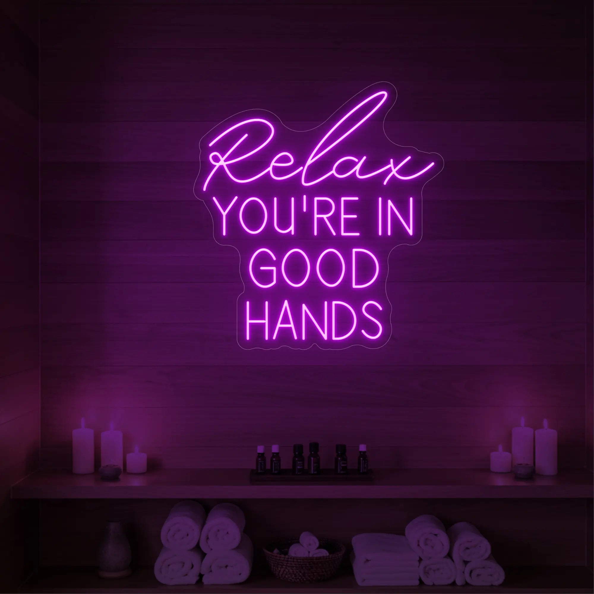 Photo of the 'Relax You're in Good Hands' neon sign glowing in deep pink against a styled interior wall.