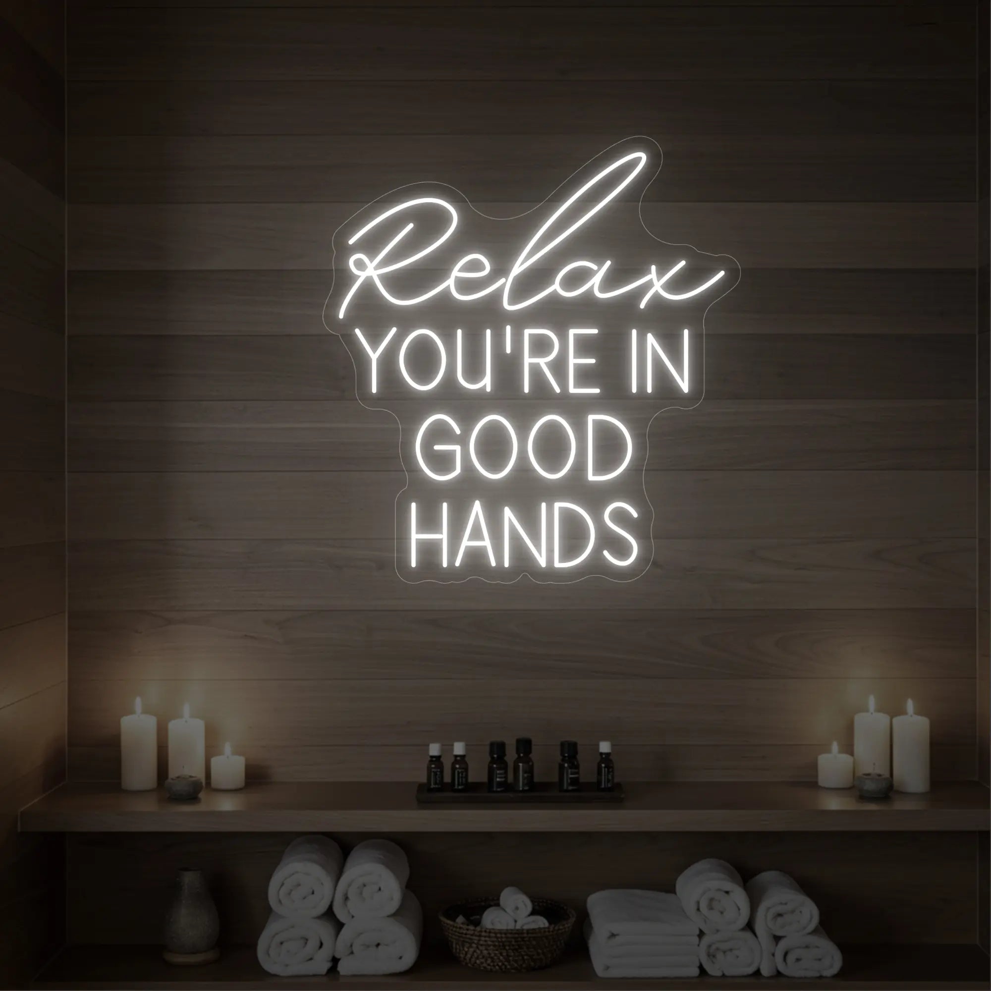 Photo of the 'Relax You're in Good Hands' neon sign glowing in cool white against a styled interior wall.