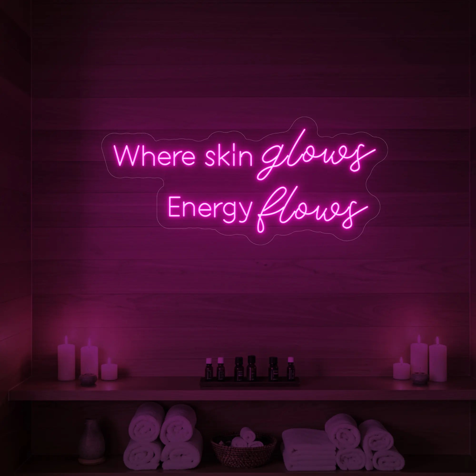 Photo of the 'Where Skin Glows, Energy Flows' neon sign glowing in light pink against a styled interior wall.