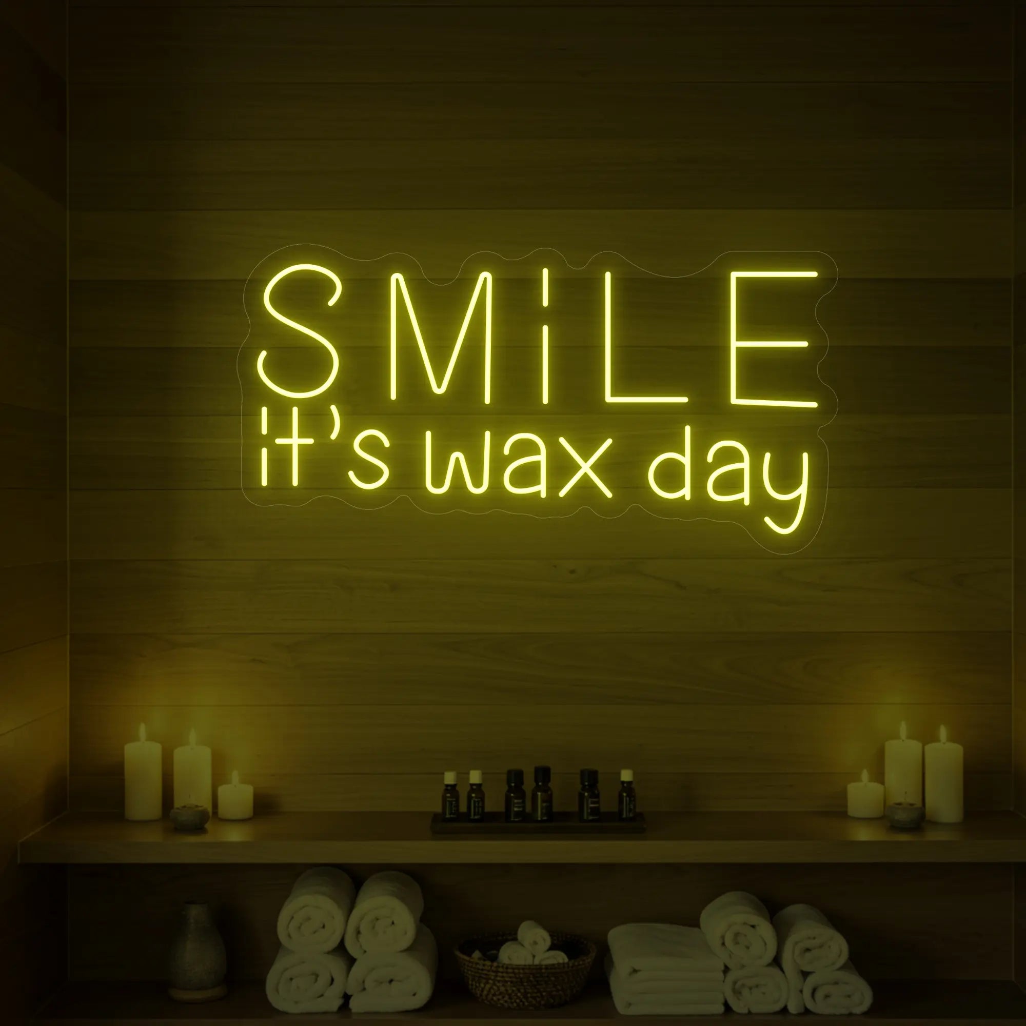 Photo of the 'Smile It’s Wax Day' neon sign glowing in lemon yellow against a styled interior wall.