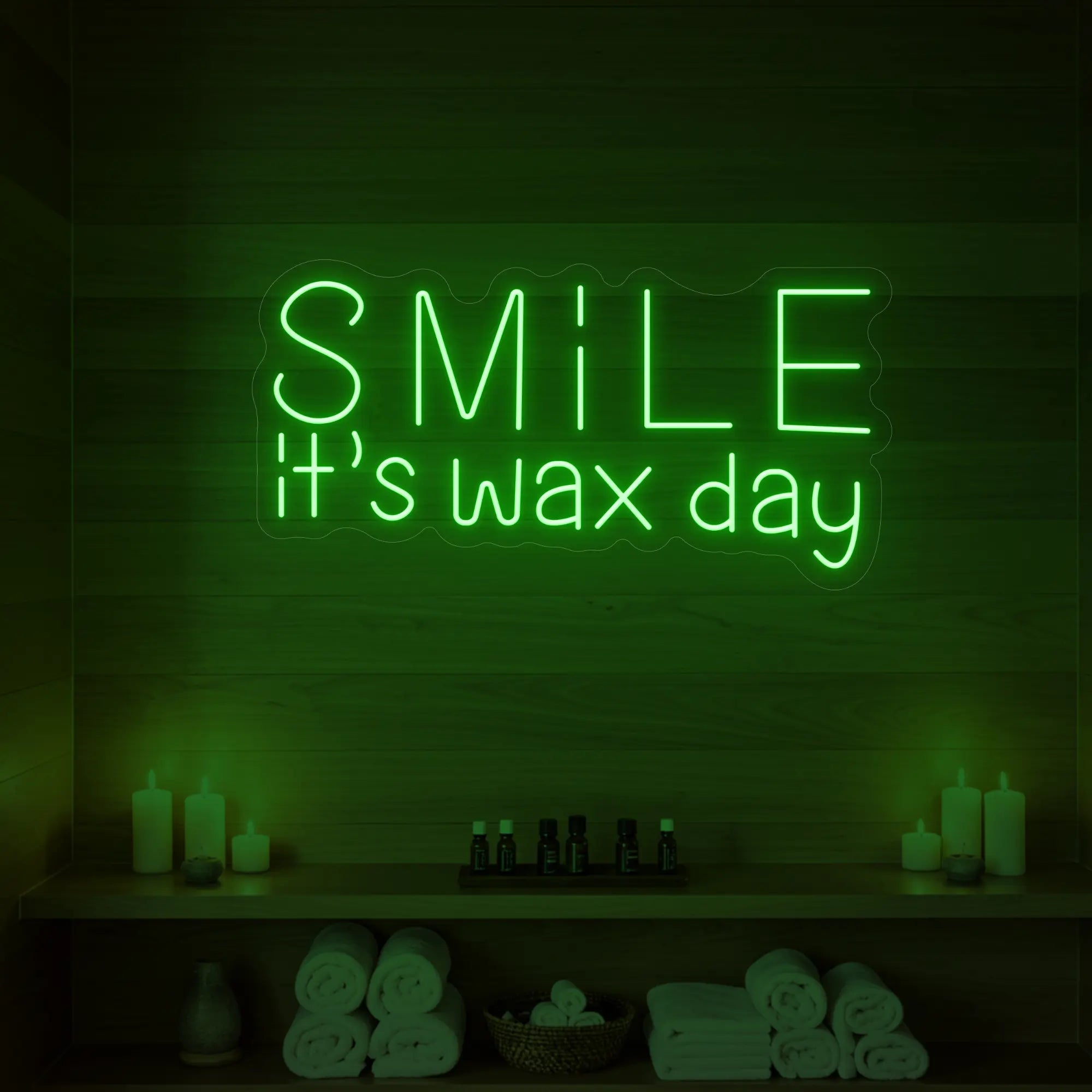 Photo of the 'Smile It’s Wax Day' neon sign glowing in green against a styled interior wall.