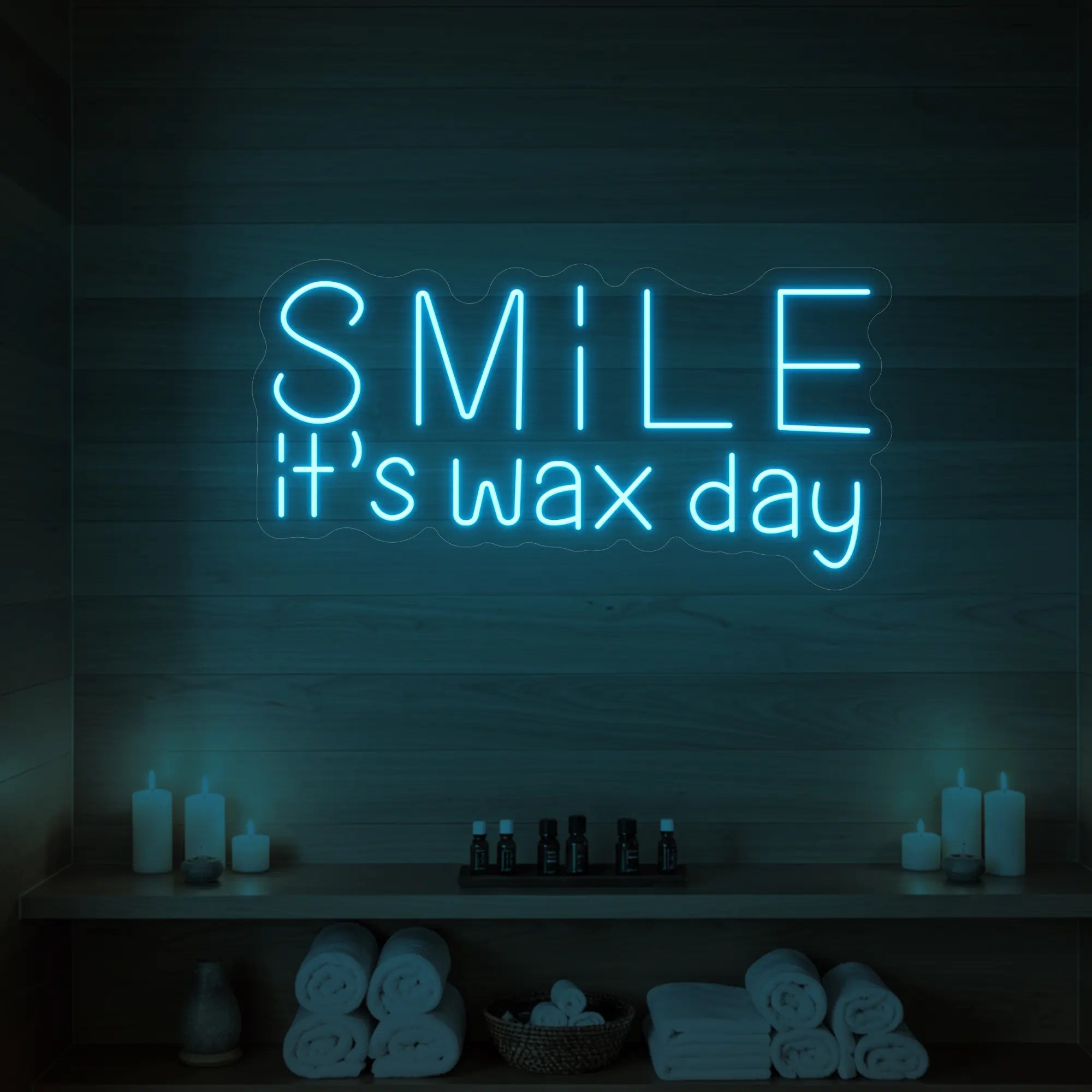 Photo of the 'Smile It’s Wax Day' neon sign glowing in ice blue against a styled interior wall.