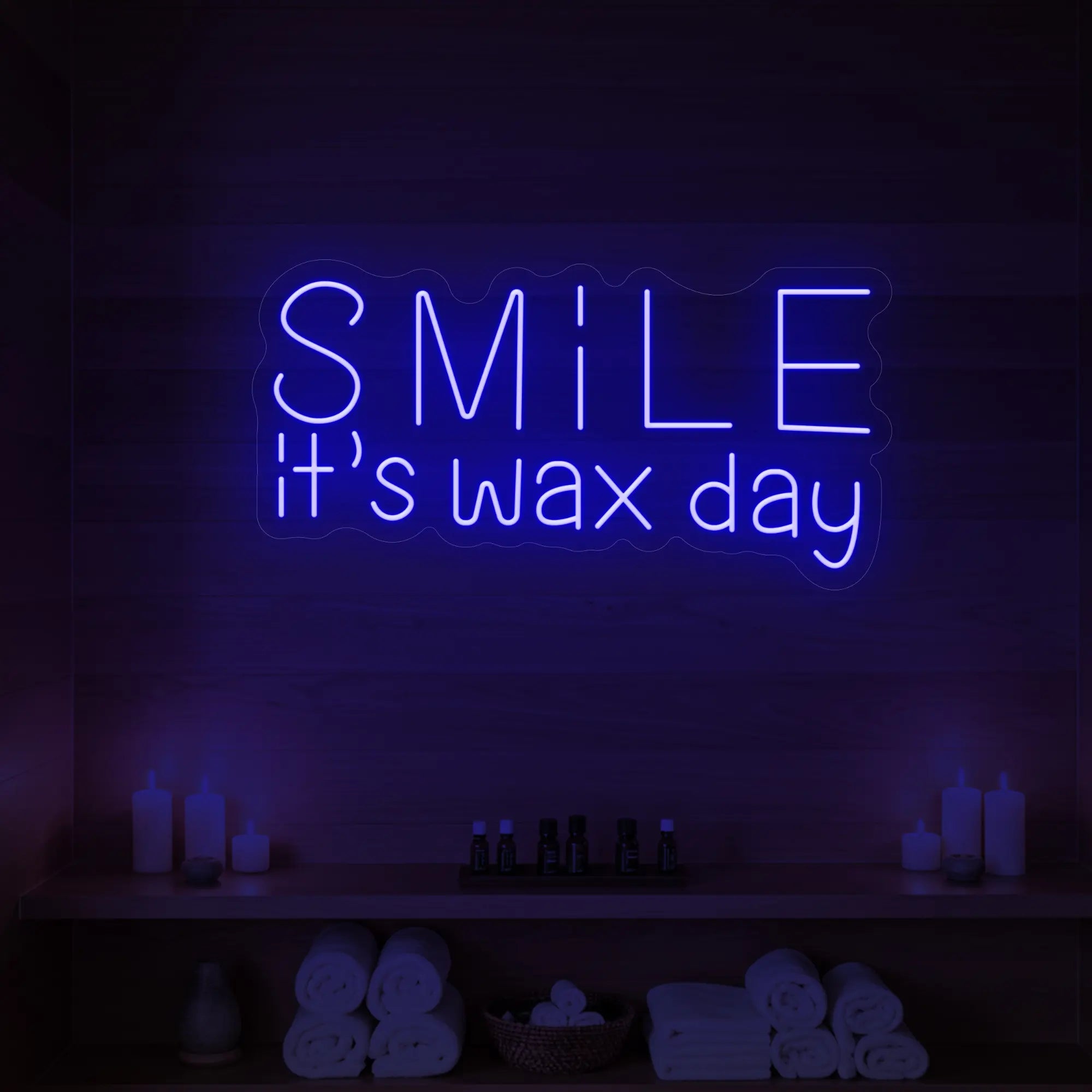 Photo of the 'Smile It’s Wax Day' neon sign glowing in deep blue against a styled interior wall.