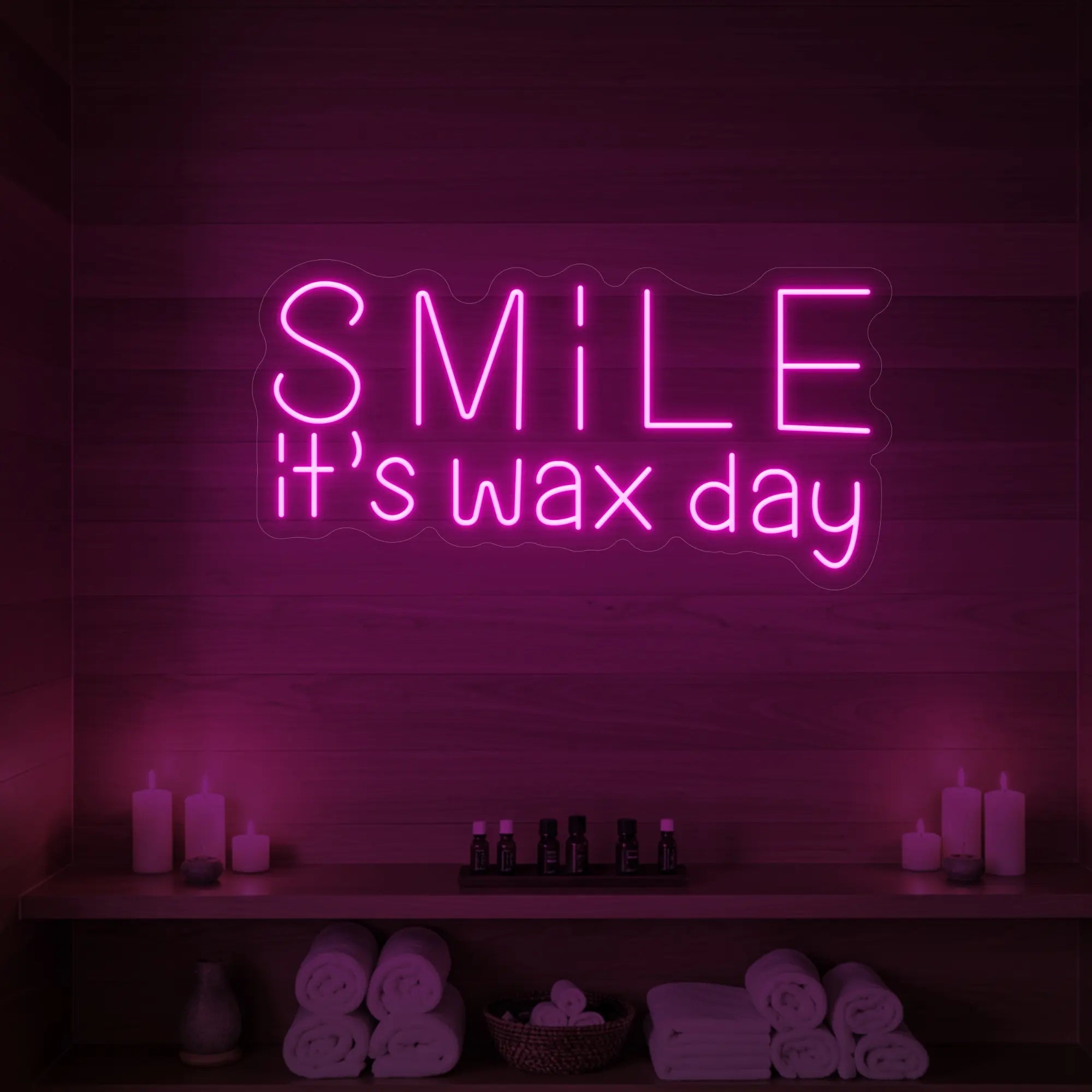 Photo of the 'Smile It’s Wax Day' neon sign glowing in light pink against a styled interior wall.