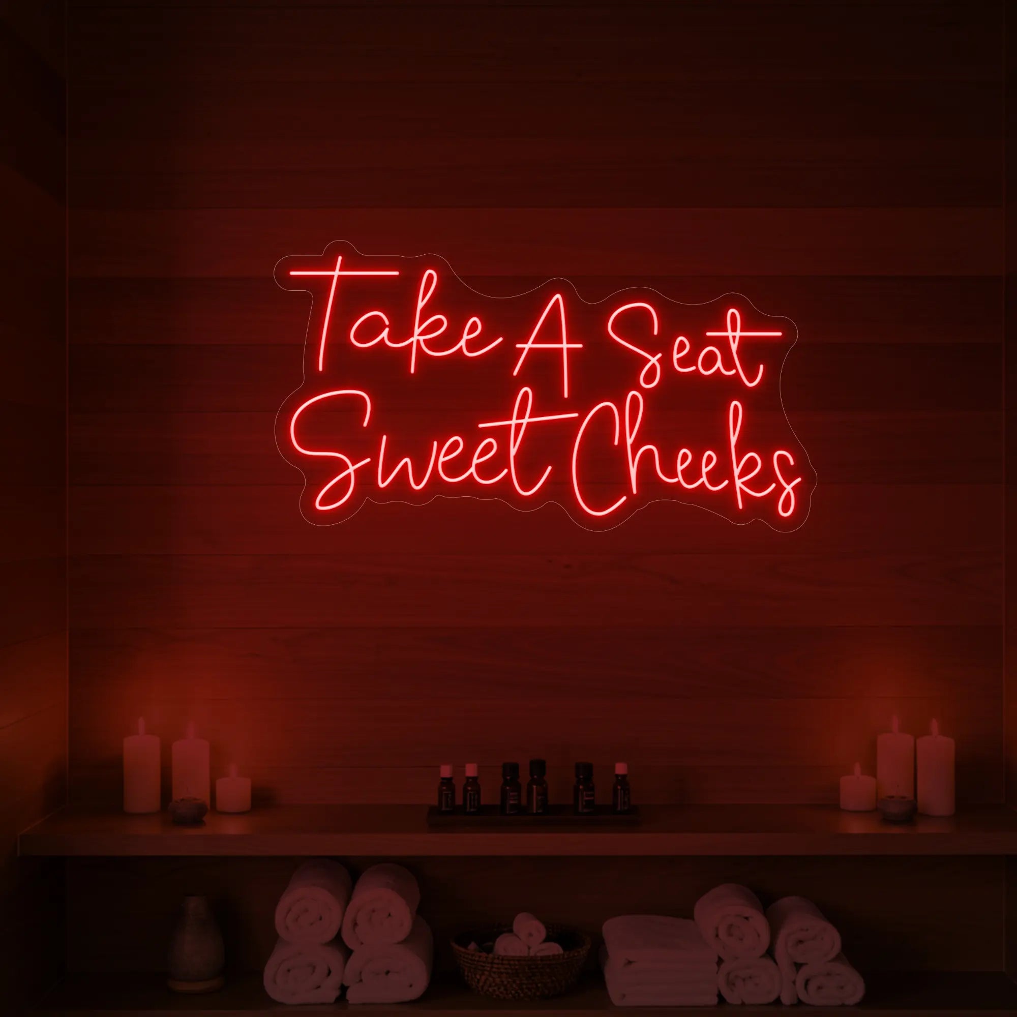 Photo of the 'Take A Seat Sweet Cheeks' neon sign glowing in red against a styled interior wall.