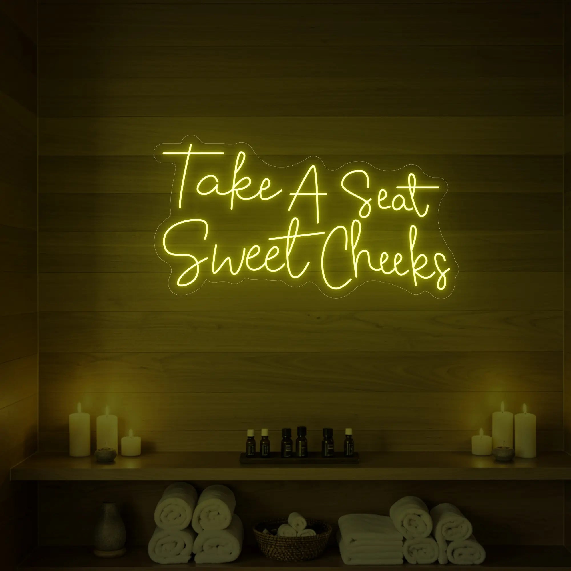 Photo of the 'Take A Seat Sweet Cheeks' neon sign glowing in lemon yellow against a styled interior wall.