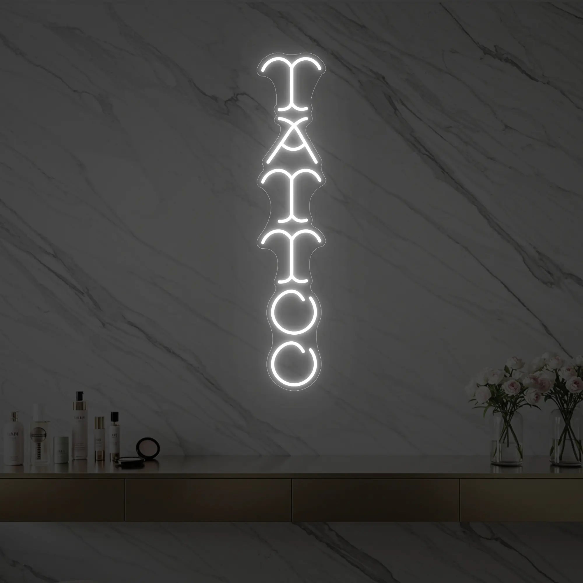 Photo of the 'Vertical Tattoo' neon sign glowing in cool white against a styled interior wall.