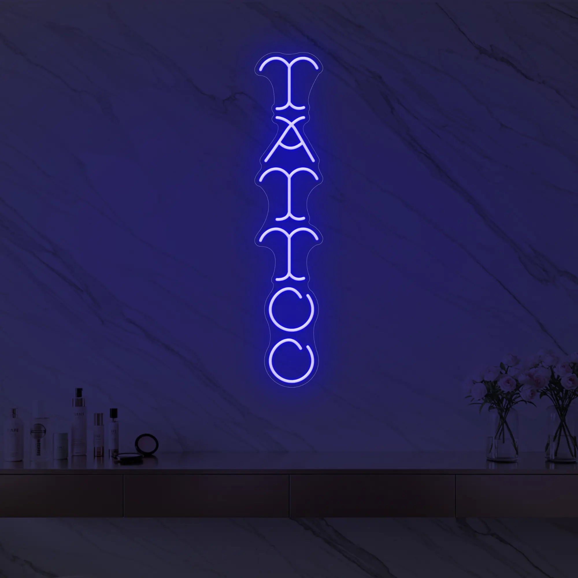 Photo of the 'Vertical Tattoo' neon sign glowing in deep blue against a styled interior wall.