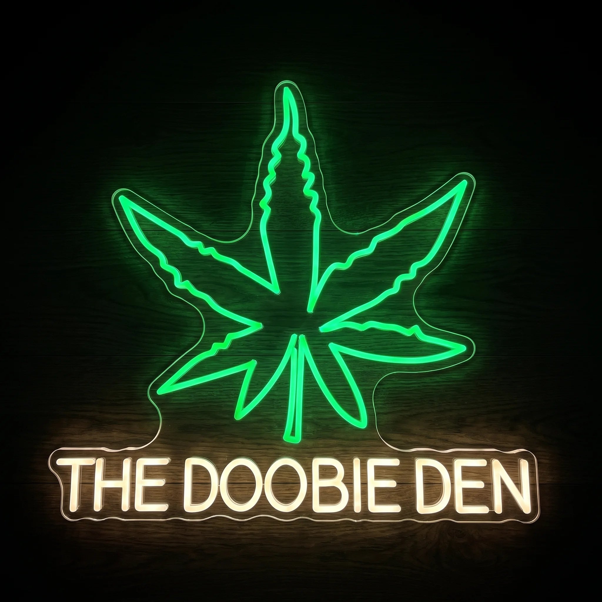 The Doobie Den LED neon sign on clear acrylic backing with a green cannabis leaf and warm white lettering for cannabis-themed wall dΓ©cor.