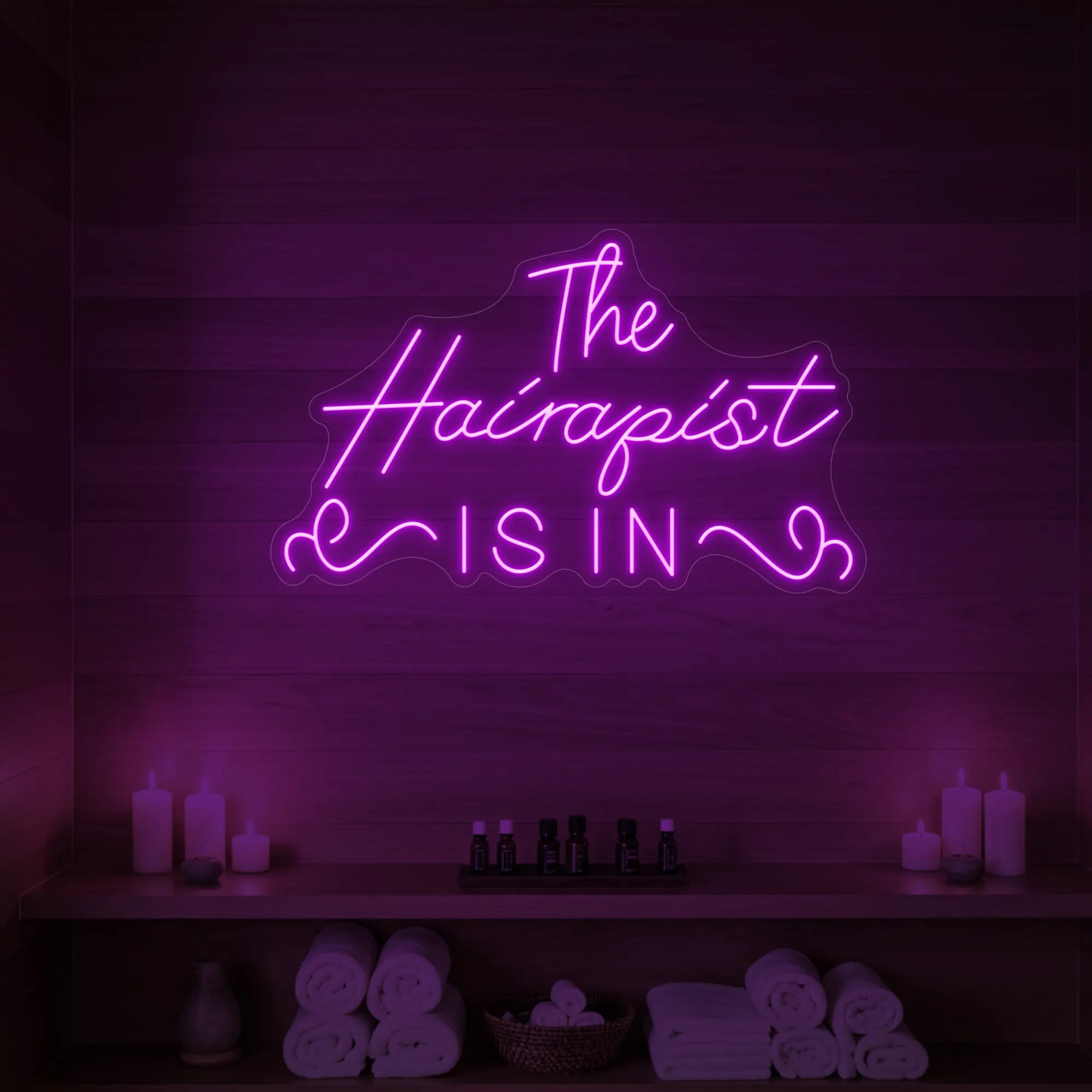 Photo of the 'The Hairapist Is In' neon sign glowing in deep pink against a styled interior wall.