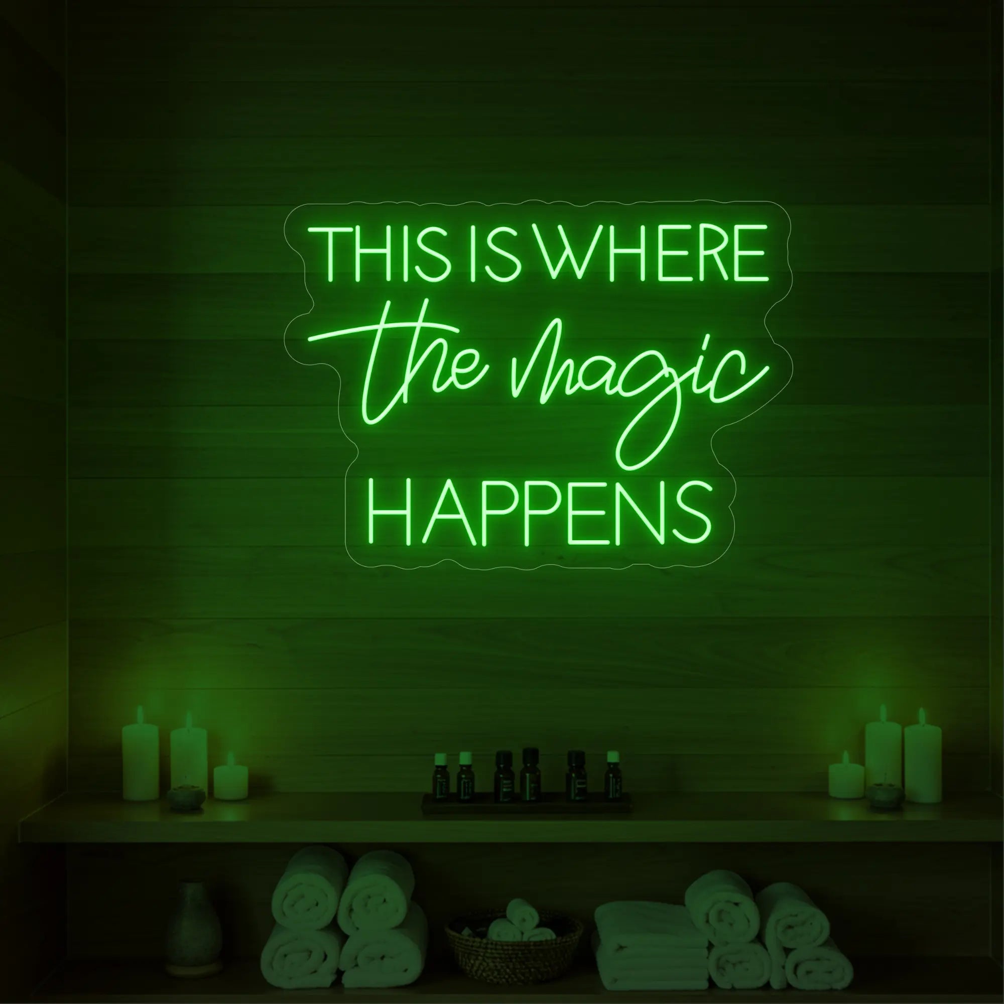 Photo of the 'This Is Where The Magic Happens' neon sign glowing in green against a styled interior wall.