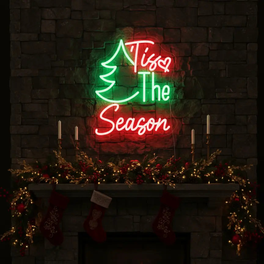 Photo of the ‘Tis The Season with Pine Tree’ neon sign glowing in multicolor against a styled interior wall.