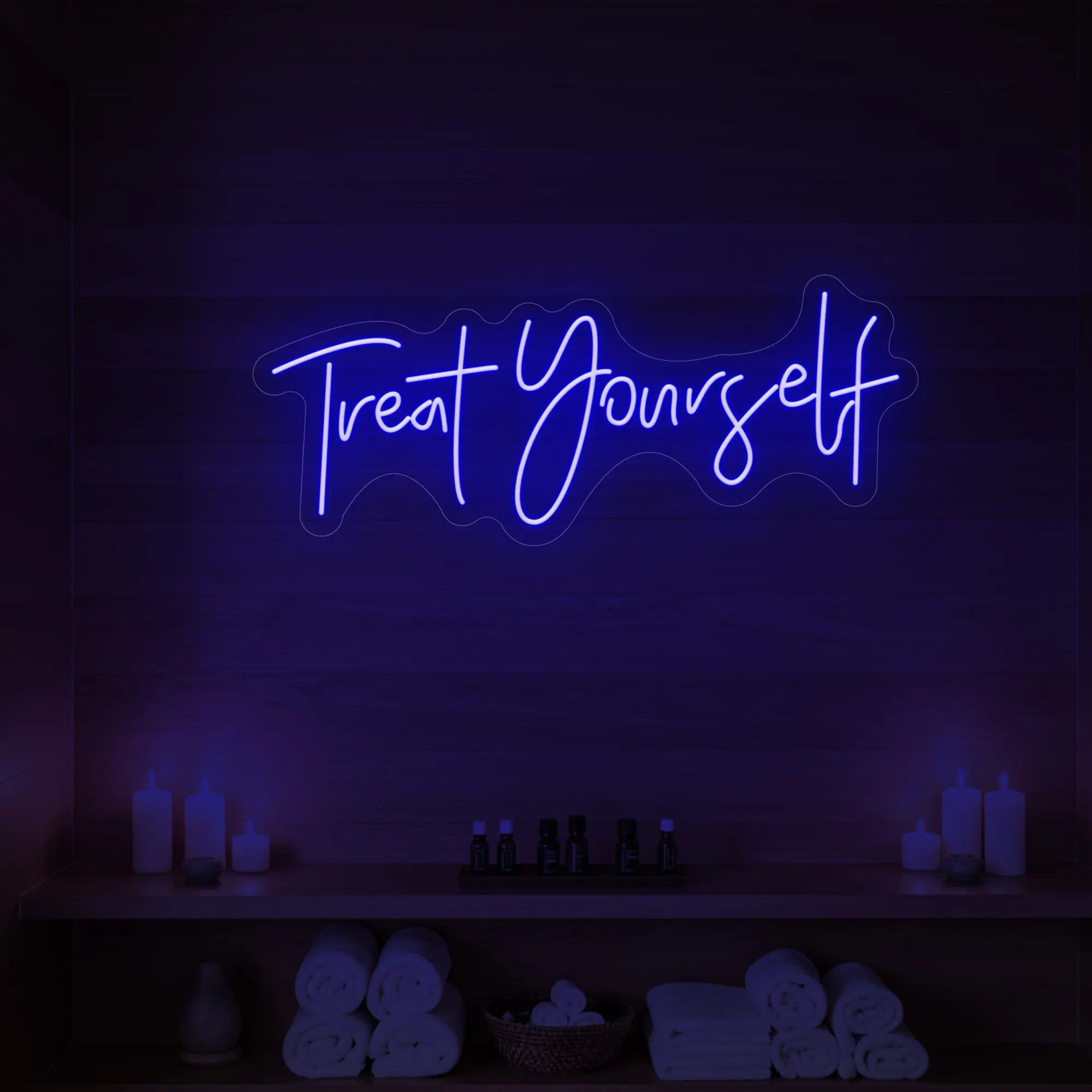 Photo of the 'Treat Yourself' neon sign glowing in deep blue against a styled interior wall.