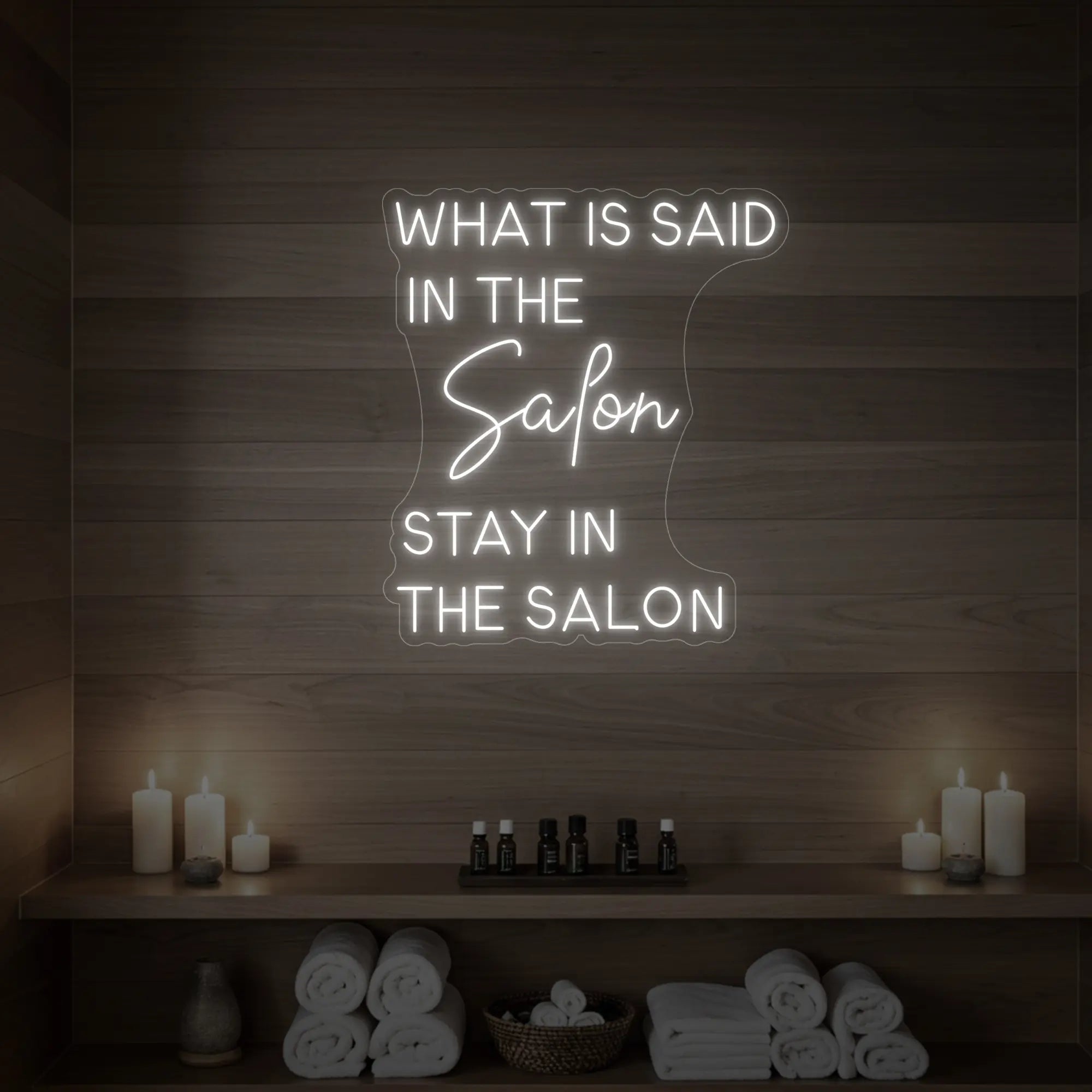 Photo of the 'WHAT IS SAID IN THE SALON STAY IN THE SALON' neon sign glowing in cool white against a styled interior wall.