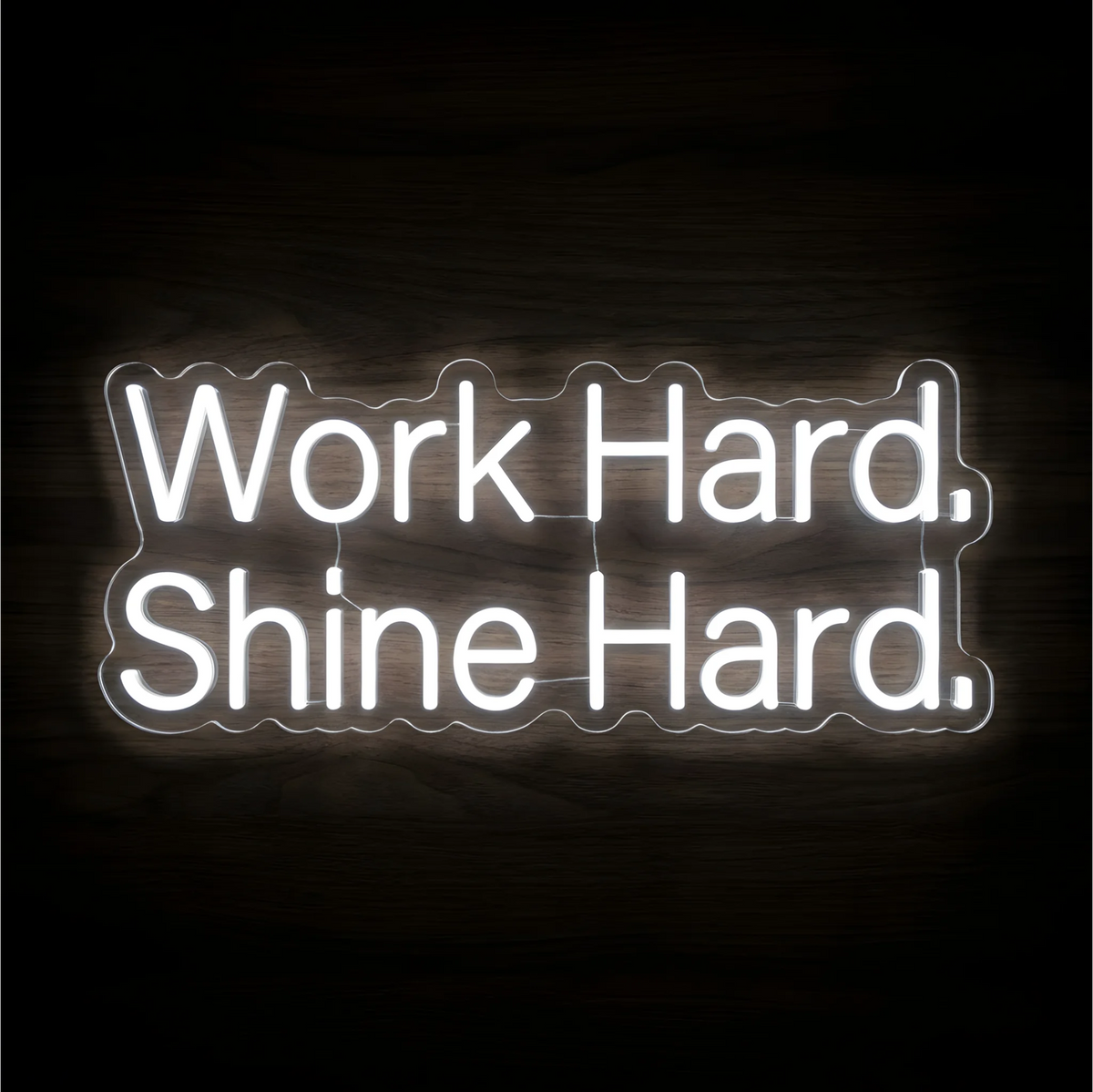 Work Hard Shine Hard LED Neon Sign with bright white lettering on clear acrylic against a dark wood background, suited to home offices and motivational workspaces.