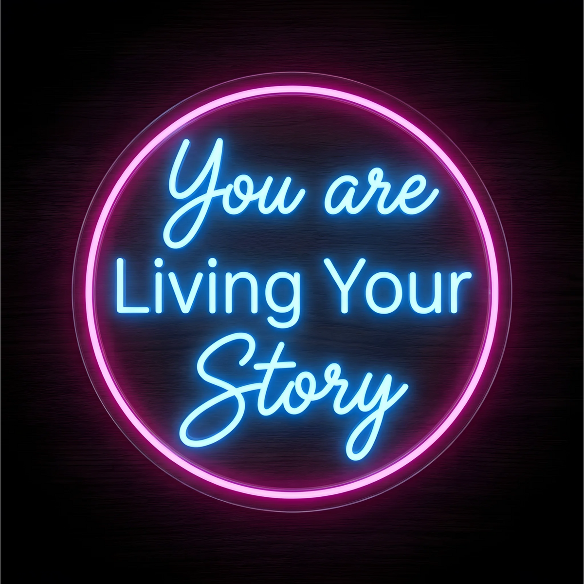 “You are Living Your Story” LED Neon Sign with bright blue lettering inside a glowing pink circular outline on clear acrylic backing against a dark wood background, suited to bedrooms and creative studios.