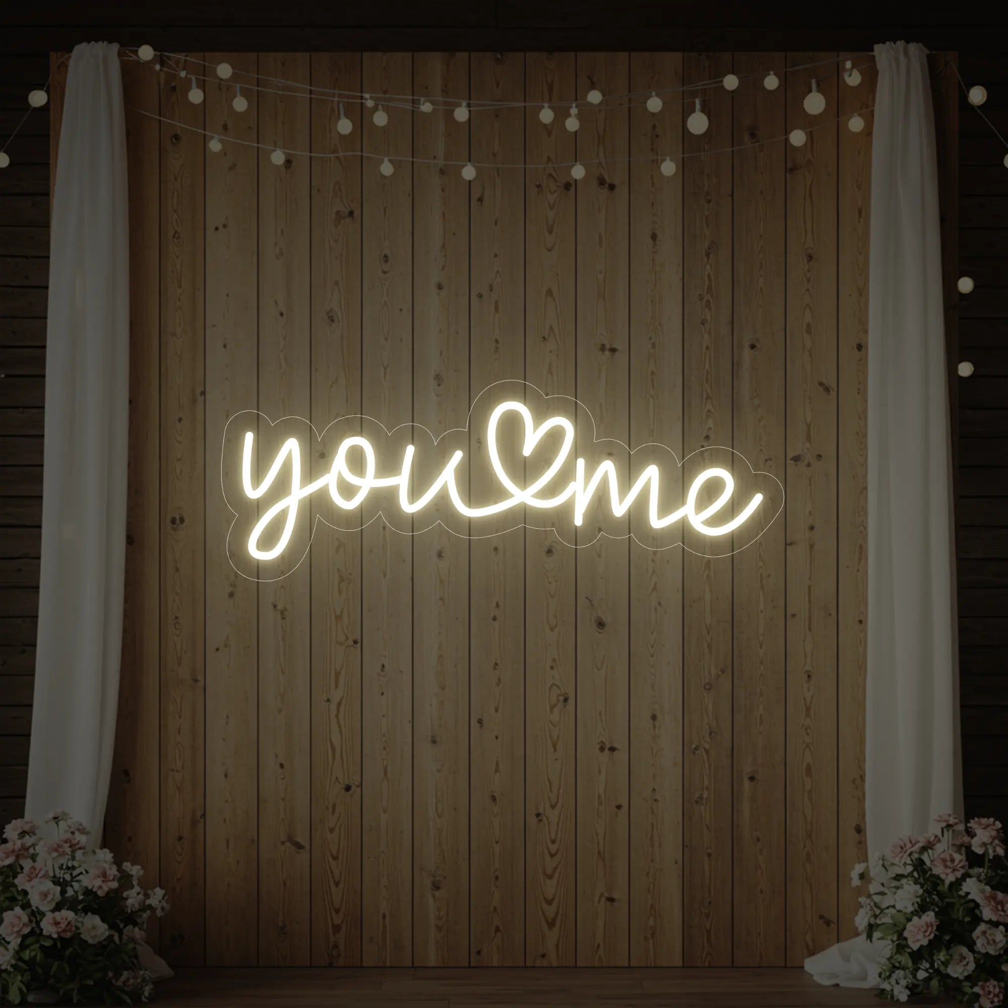 'You Heart Me' neon sign glowing in warm white against a styled interior wall.