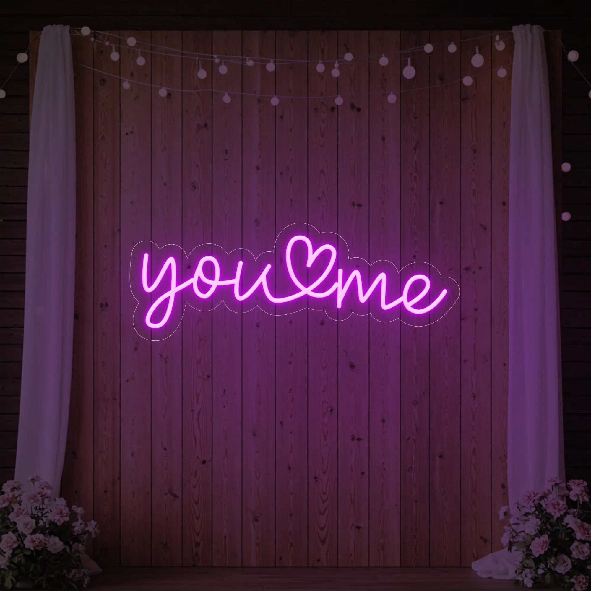 'You Heart Me' neon sign glowing in deep pink against a styled interior wall.