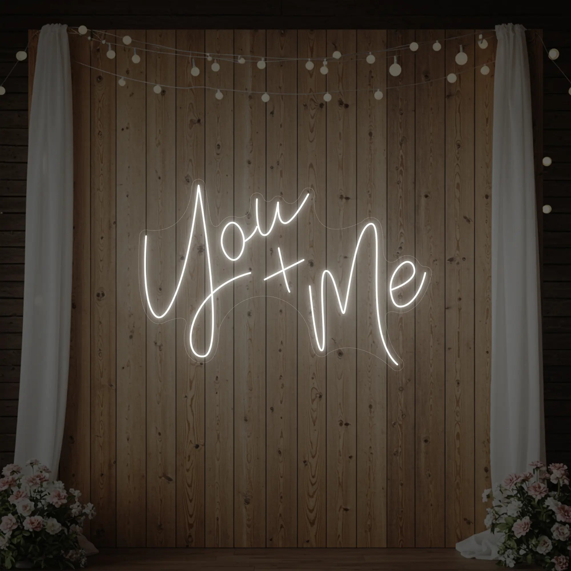 'You + Me' neon sign glowing in cool white against a styled interior wall.
