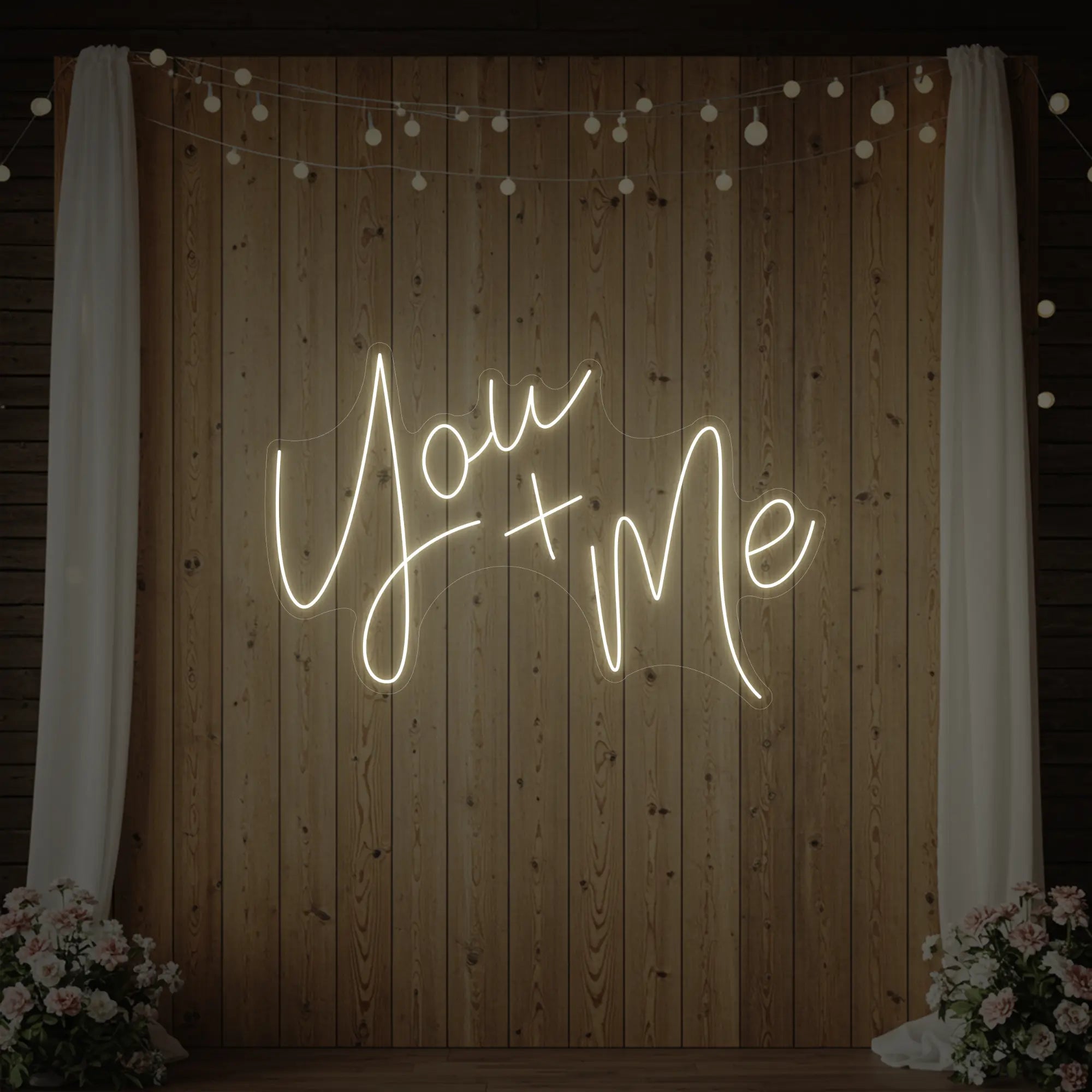 'You + Me' neon sign glowing in warm white against a styled interior wall.
