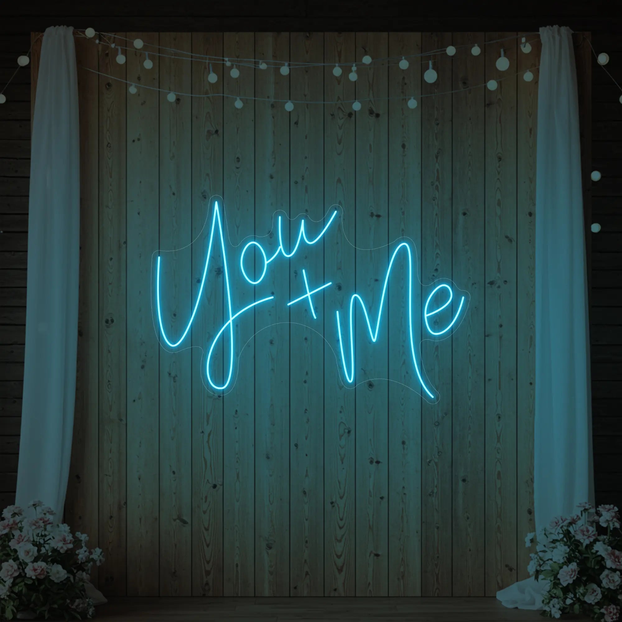 'You + Me' neon sign glowing in ice blue against a styled interior wall.