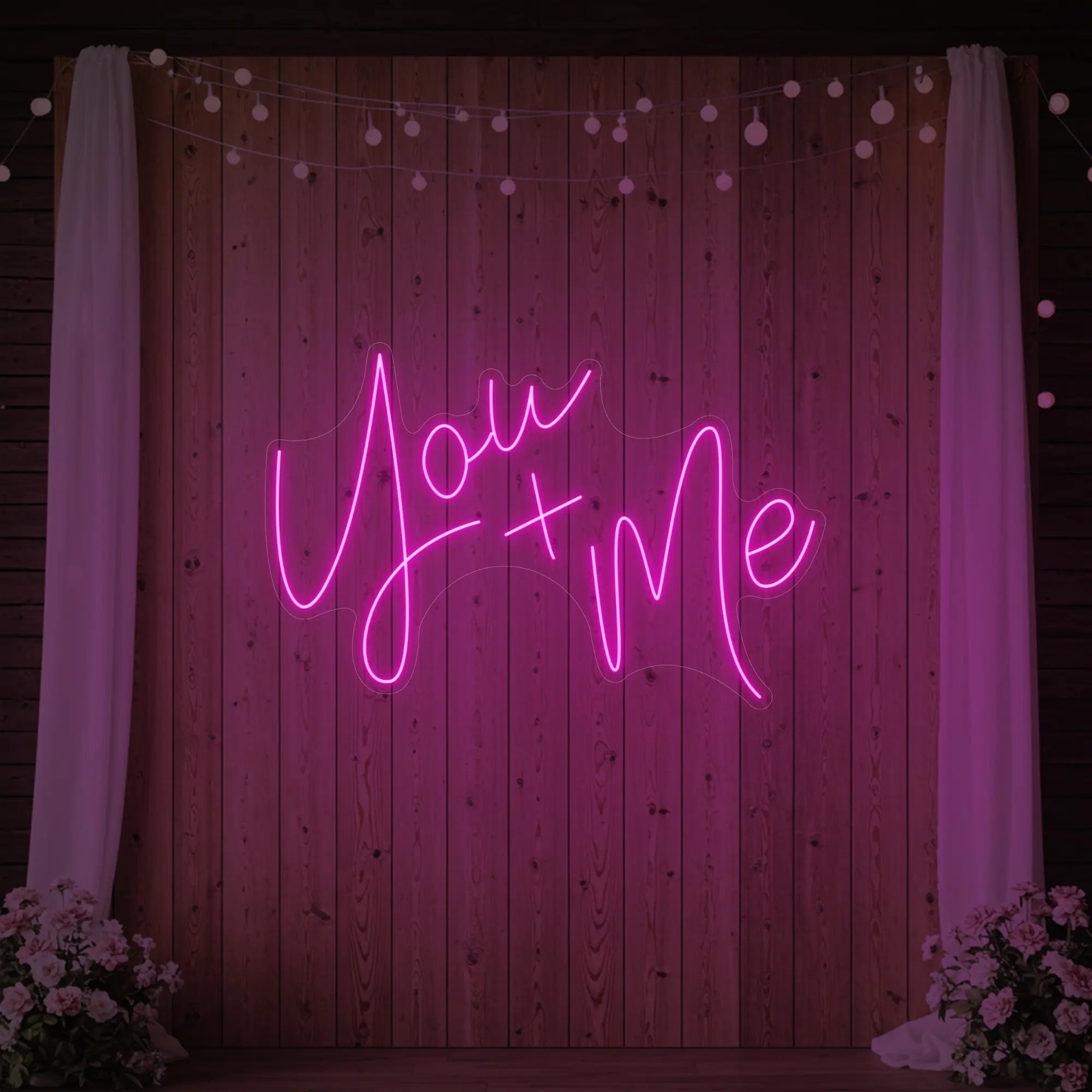 'You + Me' neon sign glowing in light pink against a styled interior wall.